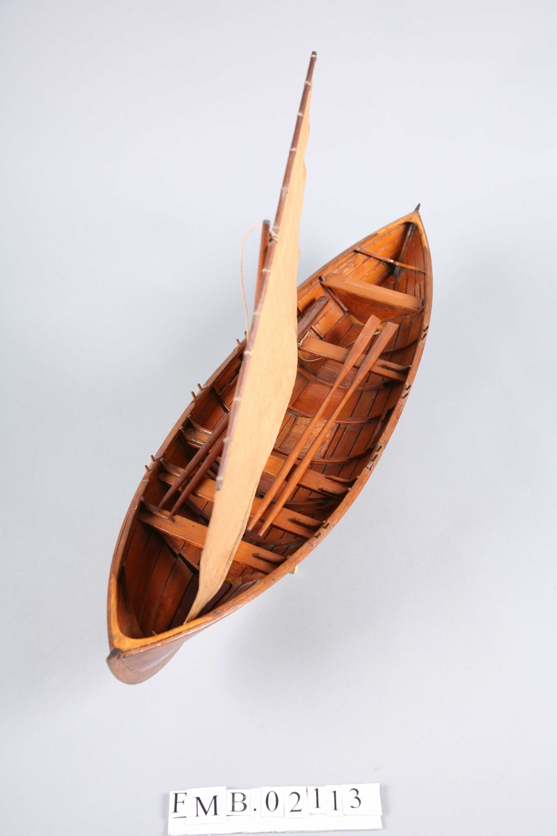 Sjekte med mast, seil og 4 årer. Den har 6 par tollepinner. Båtmodellen står på en støtte (krybbe).