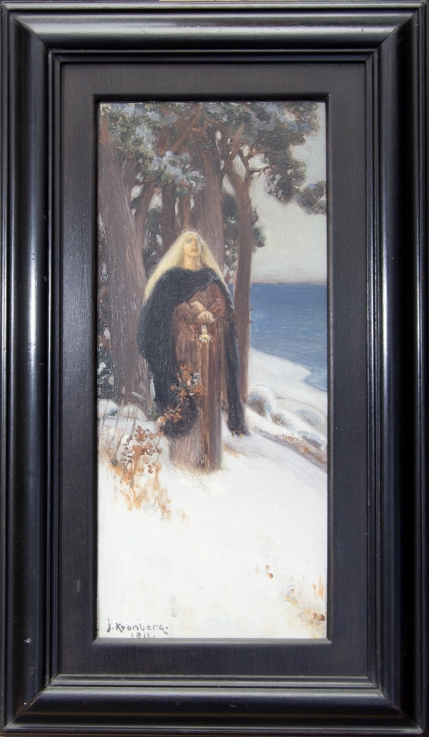Ung kvinna, helfigur, med lång rödbrun klänning och lång svart kappa stående i dagsljus i ett snötäckt landskap med tallar och sjö.