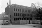 Gummifabrikens nya huvudkontor i sydöstra hörnet Joh Kocksgatan/Nygatan (idag 2016 Henry Dunkers gata) under uppförande hösten 1940. I bakgrunden skymtar Ångcentralen och fabriksskorstenen.