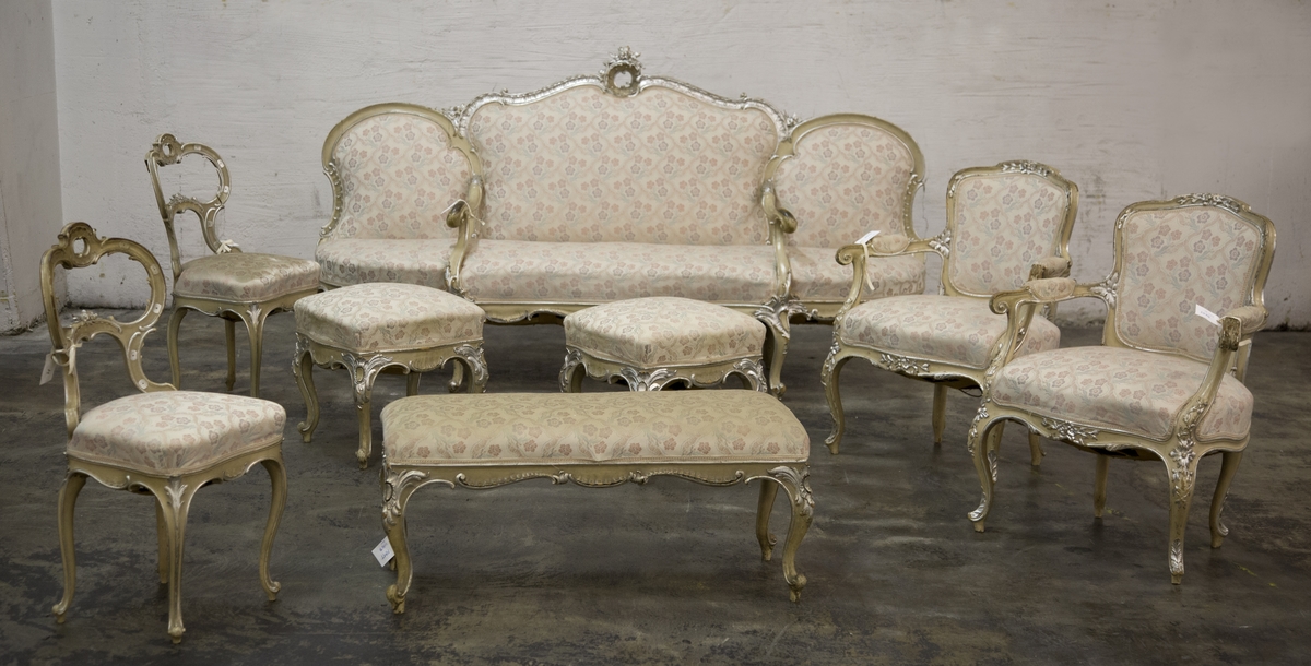 Sittemøbel for flere personer. Nyrokokko. Canapé à confidente - type, d.v.s. på hver side avsluttet av et sidesete. Alt treverk malt lyst grått med forsølvede ornamenter. Høy, stoppet rygg. Spiralfjærer både i sete og rygg. Trukket med tykk, rosa silke med ivevete, flerfargete blomster.
6 cabrioleben. de to forbena har øverst utskåret rocaille - lignende motiv med små blomster. Et glatt, åpent armlene på hver side av midtstykket.