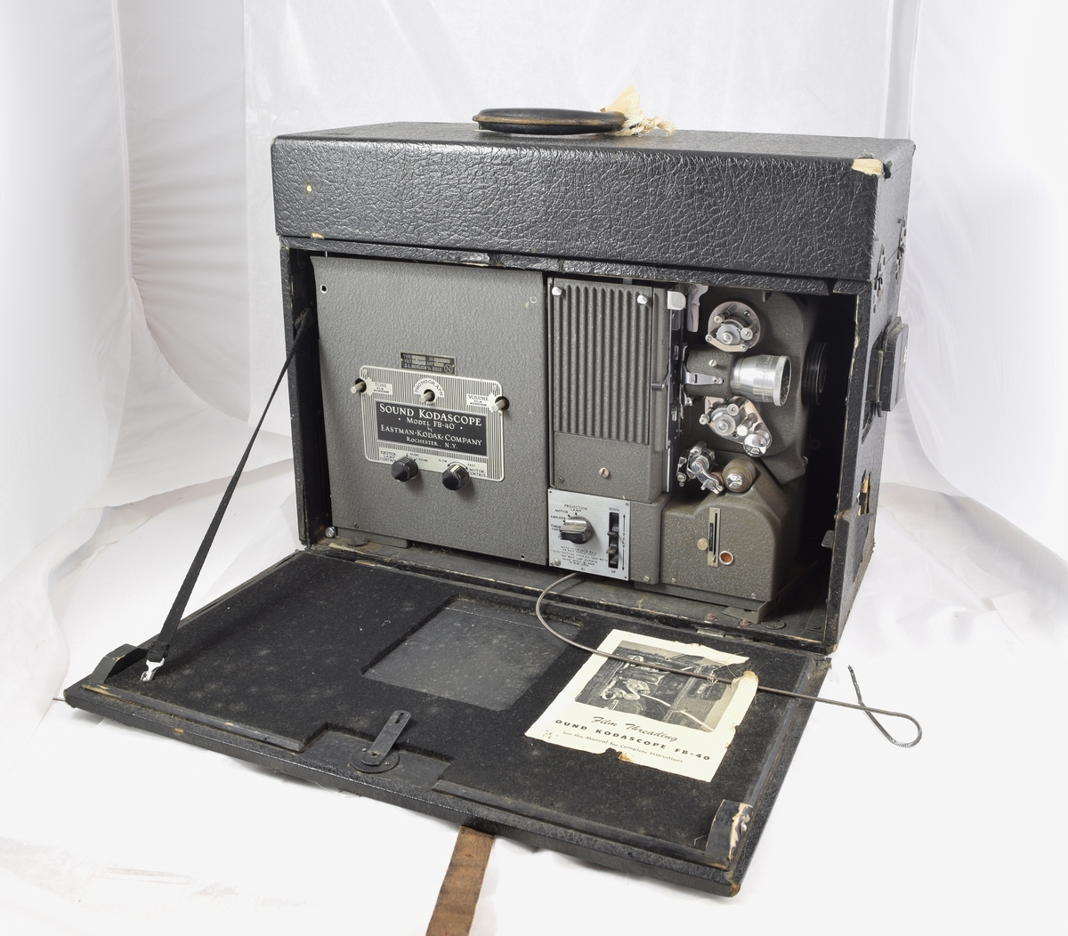Filmfremviser til filmruller. Filmen tres gjennomapparatet som vist på arket på eskens innside. Rektangulær koffert rundt apparatet med luker som kan åpnes der det er behov. (Høyttalere kommer i tillegg - se referanser.)