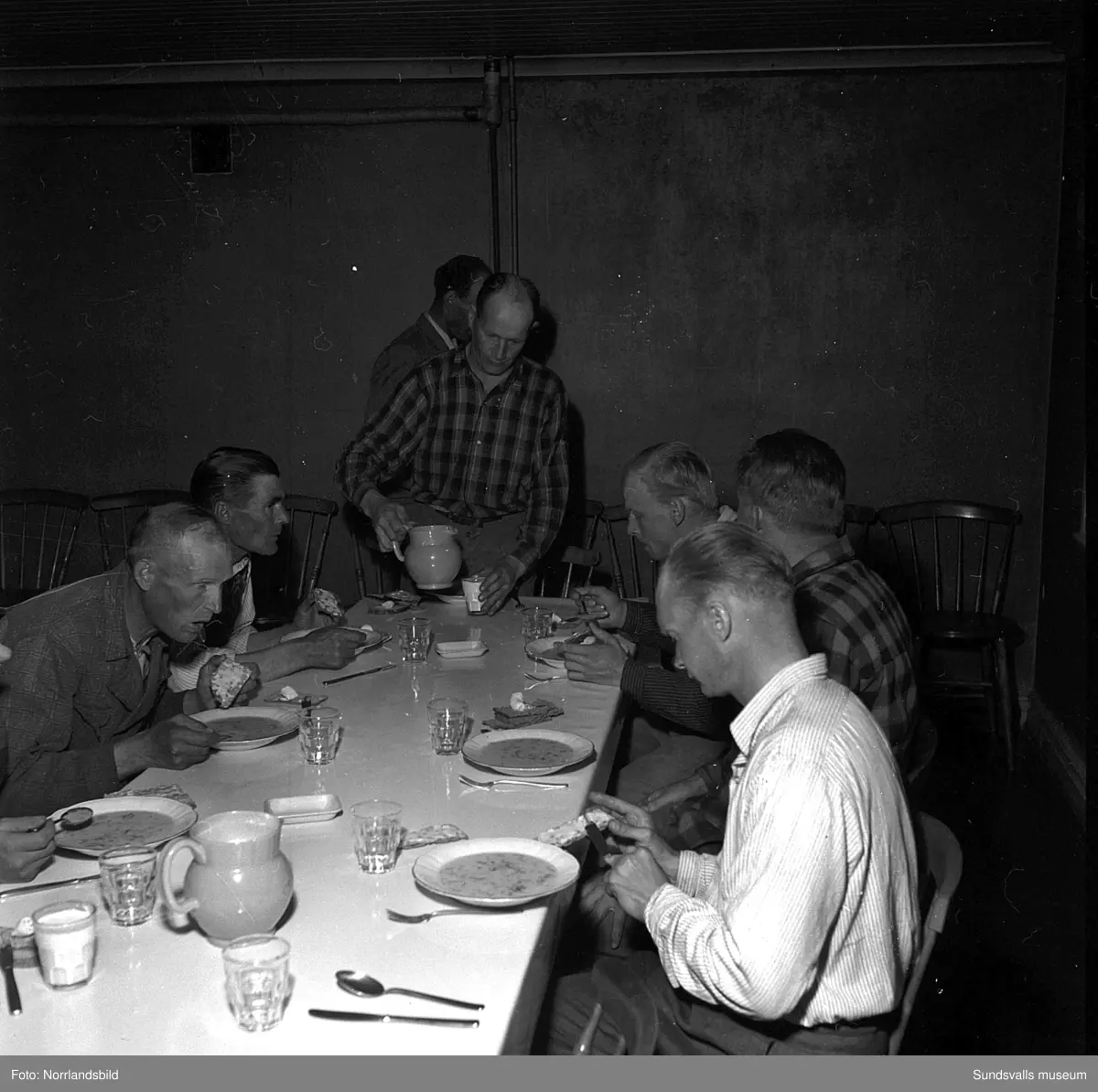 Sommaren 1951 anlände tolv finländska arbetare med båten Ragne till Sundsvall för att jobba vid Ortvikens sulfitfabrik. En välkommen förstärkning i tider då det var ont om arbetskraft. Som tillfällig förläggning användes Skönsbergs Folkets hus där den så kallade B-salen förvandlats till logement med tältsängar och i D-salen en trappa ned serverades maten. På den första bilden är det plåtslagaren Urhi Karlsson från Gamla Karleby som serveras spenatsoppa av Helga Rödén. På bild tre är det Eino Havu från Björneborg, till höger, som byter om efter sin första arbetsdag vid Ortviken.