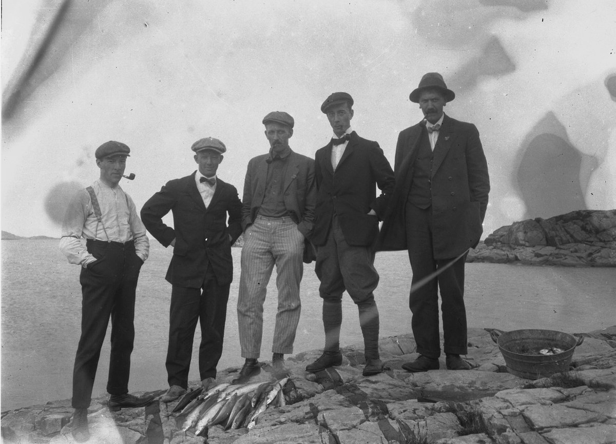 Ukjende menn med fiskefangst ved sjøen.