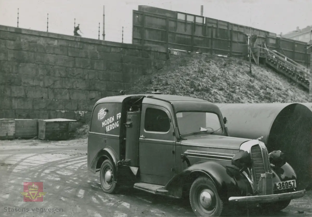 "Karbidgenerator produsert av Øveråsens Motorfabrikk, Gjøvik. De ble montert av Colbjørnsens & Co. A/S under hele krigstiden." I følge merking i album. På bilen med kjennetegn C-12178 står det skrevet "A/S Norske Konfektionsfabriker." På skiltet øverst på murbygningen står sannsynligvis "A/S Sveiseindustri." 

Bilde 1/4 er en Chevrolet med en eldre Chev. baklykt  på taket. 20.08.2016: "Bilde 1 er en Chevrolet 1939-40 varebil med norskbygd karosseri. "25.06.2018: Til venstre snuten av en Packard fra sent 1930-tall. Opplysninger fra Ivar Erlend Stav.
Klikk på pilen til høyre:
Bilde 2/4 er en Dodge 1935-1936 modell. (Strømmenbygd?)
Bilde 3/4  er en 1930 modell Brockway. 25.06.2018: Bildet 3 viser snuten av en Plymouth1937. Opplysninger fra Ivar Erlend Stav.
Bilde 4/4 er en Ford fra 1937-1938 modell." 25.06.2018:  "Ford 1938, siden det var første år med langsgående blanklist hos Ford. Karosseriet er originalt amerikansk varebilkarosseri på personbilchassis ("sedan delivery" - i motsetning til et mer grovbygd varekarosseri på lett lastebilchassis og lastebilfront, kalt "panel delivery". Opplysninger fra Ivar Erlend Stav. 

17.08.2016: Opplysninger til kjøretøyene på bildet v/tidligere daglig leder John Hindklev ved Norsk Kjøretøyhistorisk Museum. 

"Under andre verdenskrig besto virksomheten til firmaet Colbjørnsen stort sett av å montere og vedlikeholde karbidgeneratorer fra Øveråsen. Legg merke til hvordan man felte generatorene inn i varebilkarosseriene. Reklameteksten  ble delvis borte." Sitat fra boka: "Familiefirmaet-utenom allfarvei/2000 årsboken." Colbjørnsen & Co A/S, av Bjørn Ausjen Johannessen.