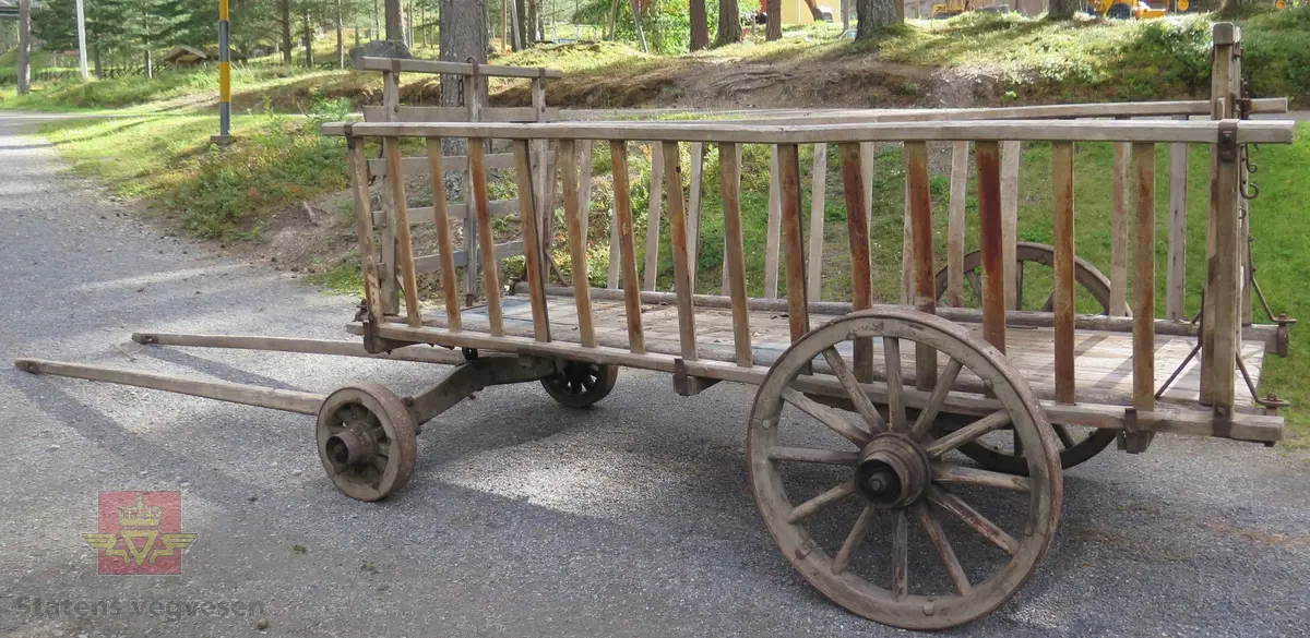 Høyvogn. med fire hjul og drag for hest. Karmer med sprinkler. Lagd av tre og metall. Har rester av blå maling.