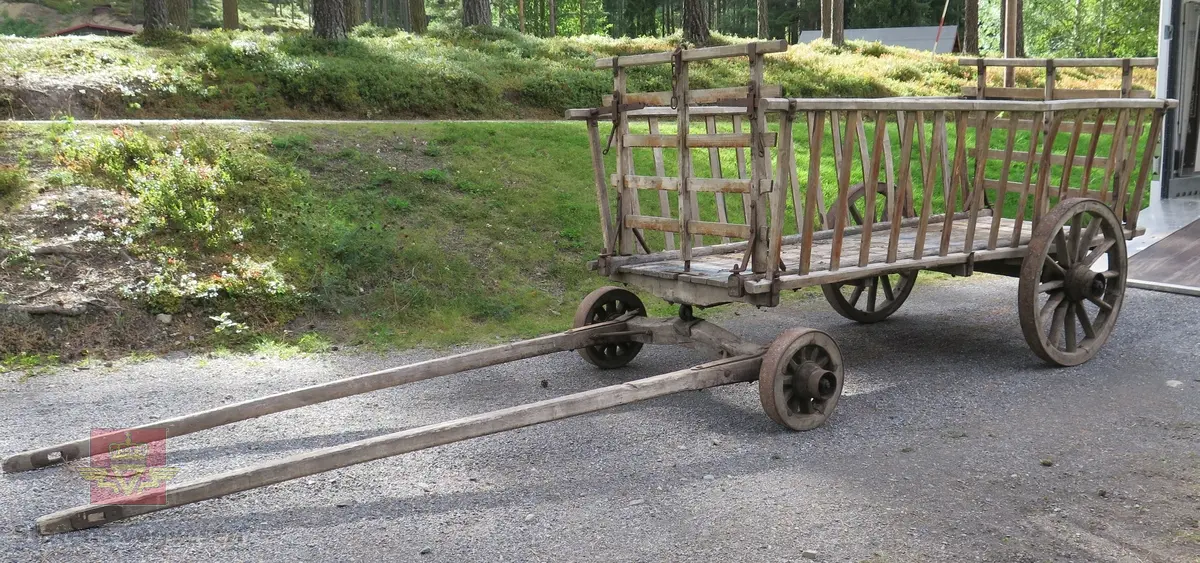 Høyvogn. med fire hjul og drag for hest. Karmer med sprinkler. Lagd av tre og metall. Har rester av blå maling.