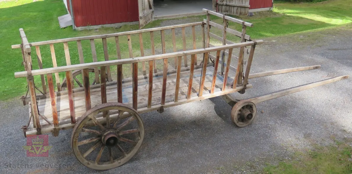 Høyvogn. med fire hjul og drag for hest. Karmer med sprinkler. Lagd av tre og metall. Har rester av blå maling.