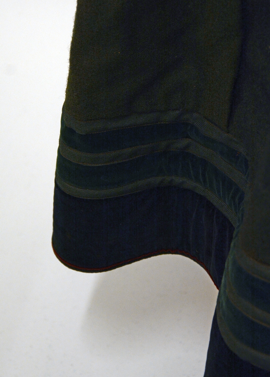 Stakk med påsydd liv. Skjørtet er rynket oppe, metallhekter på hver side av splitten/åpningen foran. Stoffet er av svart vadmel i lerretsbinding. Brodert mørkerød kant øverst på stakken. Skoningen er påsydd med et annet tøy enn det originale, den er 10 cm og har striper av mørkegrønn og sort fløyel.Skoningen er 10 cm. Nest nederste kant er mørkerød.Livet har kjøpetøy i trykteblomster med påsydde bånd. Halsutringningen er av mørkerødt fløyel med broderibord i lilla. Ermutringningene er av sort bomullstøy med mørkerød broderibord. Fòret er av rutet bomullstøy. Stakketøyet er falmet, har noen flekker,og små hull etter møll.