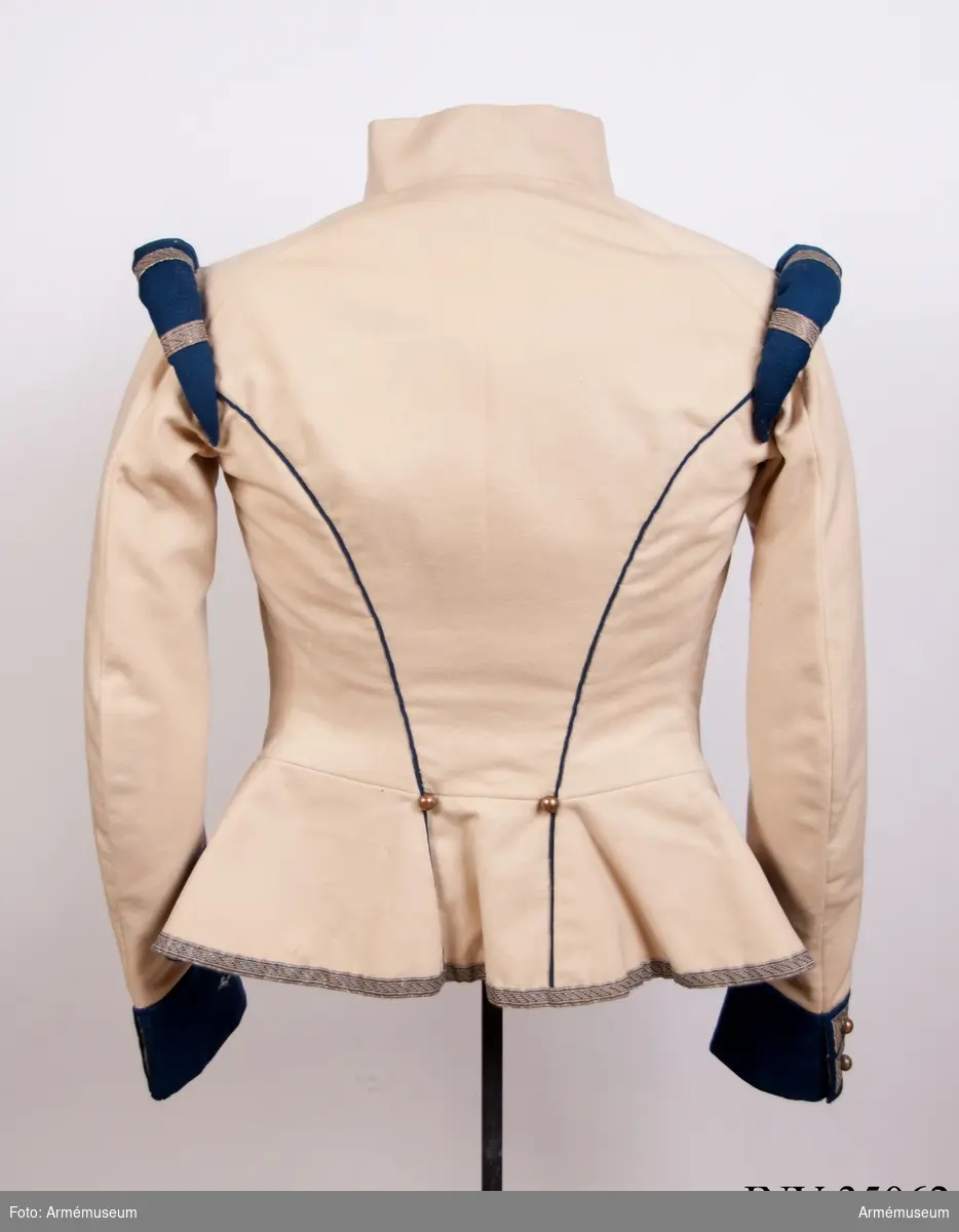 Rekonstruktion av jacka m/1781 för officer vid Lätta livdragonerna.
Jackan är sydd av vitt kläde med kragspeglar, bröstrevärer, axelkarmar och ärmuppvik i mörkblått kläde. Passpoaler av blått kläde i ryggsömmar och främre delsömmar på ärmarna.
Den är dekorerad med metallgaloner på bröstrevärer, axelkarmar och ärmuppslag, och har 16 icke funktionella kulknappar av mässing fram, samt 2 i varje ärmslut och 2 vid ryggslutet bak.
Mitt-fram-linjen är kraftigt svängd, och framstyckena är vadderade över bröstet. Jackan stängs mitt fram samt i ärmsprunden med hysk och hake. 
Den är konstruerad med avskärning i midjan, samt insnitt fram. Separata sidstycken. Skört utan slits bak.
Axelkarmarna är vadderade och står rakt upp.
Jackan är helfodrad med vitt bomullstyg.

Plaggets skärning och sömmar, de vadderade axeltungorna, de djupt skurna bröstrevärerna, uppviken, fodret m.m. indikerar ganska tydligt att den är tillverkad senare, troligen under sent 1800-tal. Även tygkvalitéerna indikerar en yngre datering.