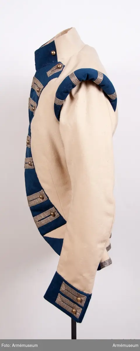 Rekonstruktion av jacka m/1781 för officer vid Lätta livdragonerna.
Jackan är sydd av vitt kläde med kragspeglar, bröstrevärer, axelkarmar och ärmuppvik i mörkblått kläde. Passpoaler av blått kläde i ryggsömmar och främre delsömmar på ärmarna.
Den är dekorerad med metallgaloner på bröstrevärer, axelkarmar och ärmuppslag, och har 16 icke funktionella kulknappar av mässing fram, samt 2 i varje ärmslut och 2 vid ryggslutet bak.
Mitt-fram-linjen är kraftigt svängd, och framstyckena är vadderade över bröstet. Jackan stängs mitt fram samt i ärmsprunden med hysk och hake. 
Den är konstruerad med avskärning i midjan, samt insnitt fram. Separata sidstycken. Skört utan slits bak.
Axelkarmarna är vadderade och står rakt upp.
Jackan är helfodrad med vitt bomullstyg.

Plaggets skärning och sömmar, de vadderade axeltungorna, de djupt skurna bröstrevärerna, uppviken, fodret m.m. indikerar ganska tydligt att den är tillverkad senare, troligen under sent 1800-tal. Även tygkvalitéerna indikerar en yngre datering.