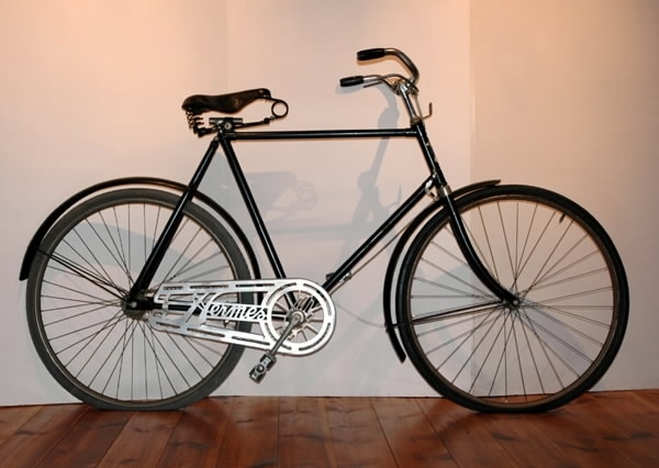 Cykel av stålrör. Diamond-ram. Spiralfjädrad lädersadel med pressat märke, text: "MANUFACTURED IN BIRMINHAM" (se bild). Styrhandtag av mönstrad celluloid. Ringklocka. På styret handtag till bakre fälgbroms. Lykthållare. Stänkskärmar av plåt. Stålfälgar, förnicklade med svart mittrand, kantad av röda linjer. Suspensionsekrar, svartmålade. Sammansatt vev. Frihjulsnav utan broms. Kedjeskydd av lättmetall, genombrutet med mönster: "Hermes". Styre, bromsinrättning, gaffelkrona och vevparti förkromade. I övrigt svart med rektanglar av röda linjer på skärmar och gaffelsidor. På styrrörets framsida en springande, fackelbärande mansgestal, runt vilken läses HERMES. Där ovan stiliserande örnvingar krönta av riksäpple. Nedanför sköld med text: "A.B. NYMANS VERKSTÄDER, UPSALA".