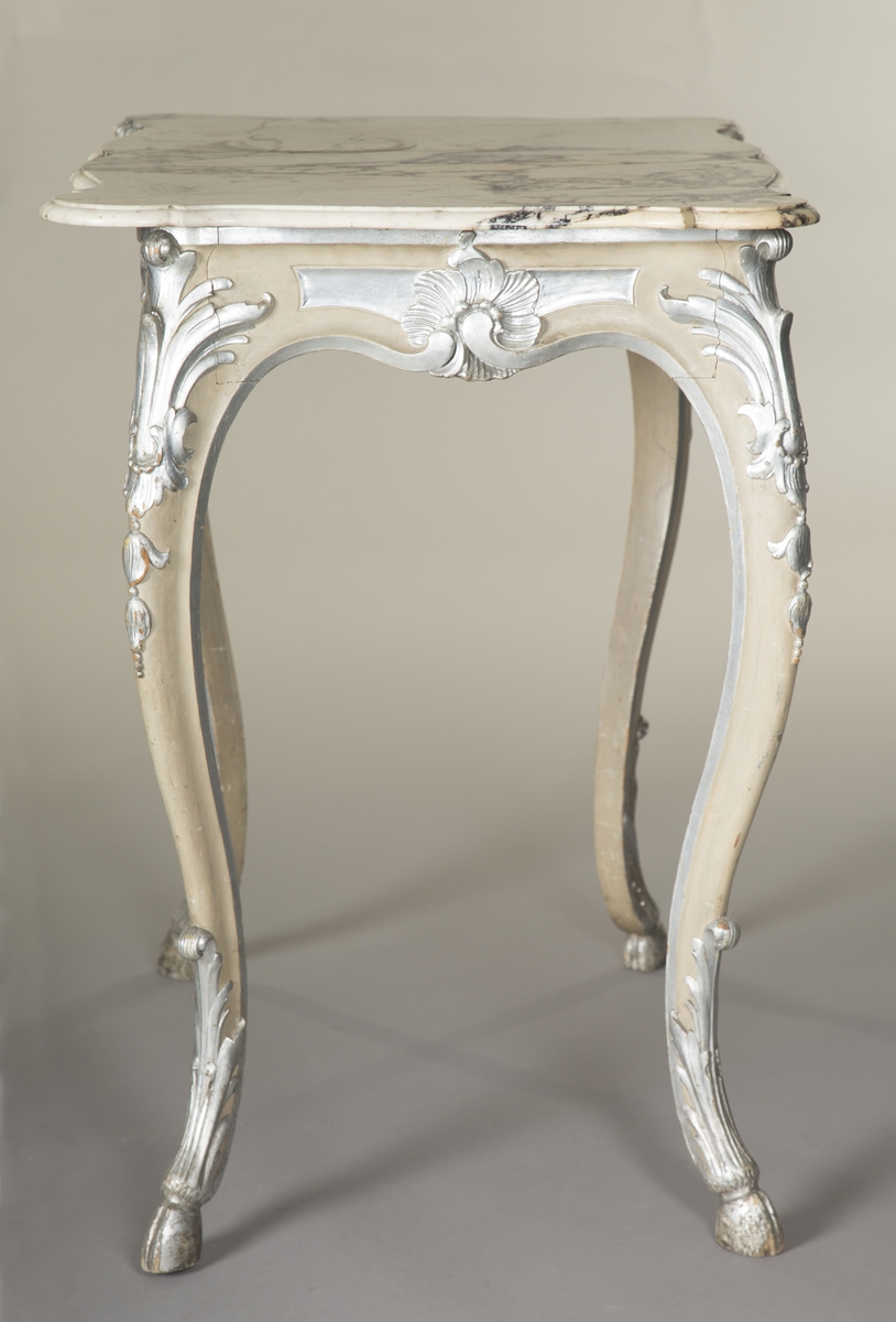 Rektangulært bord med treunderstell og marmorplate i nyrokokko. Malt lysegrått med forsølvete ornamenter. Sort og hvit marmorplate med svunget kontur. Cabrioleben med kloveavslutning. Sargens midtfelter har på kortsidene utskåret rocaille, og på langsidene skåret rankeverk. Bena har også skåret rankeverk.