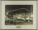 Flygplan Fokker D V.II med finsk militär märkning står i en hangar. En man står vid flygplanets vinge. Inramat foto.