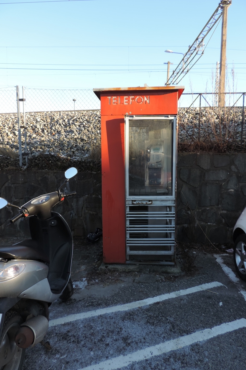 This is the story of how Norway’s most important conversation-space was designed by a young, freshly graduated man from Bergen.

“Norwegian architects are hereby invited…”
In the autumn of 1932, Oslo Telefonanlegginitiated an architectural competition. Finally, Oslo would get its own telephone booth. The city had had so called “talking-stations” from 1885, which in turn were overtaken by automatic telephones 
 only available at selected Narvesen kiosks. The state 
was of the opinion that now was the time to offer the public a better service; public telephone booths open 24/7, like the ones they already had in Sweden and England. But what would they look like, these new telephone booths? What considerations would it
 be necessary to take when designing it? The telegraph board developed a detailed list of demands and restraints: “The booth is intended to be placed outside on the streets and squares and need to be designed so that snow and ice does not hinder the opening and closing of the doors,” they wrote. “To prevent vandalism, theft, uncleanliness etc. inside the booth, it needs to be designed so that from all angles one may see what is going on in there.” Additionally, it would need to withstand storms and bad weather, and “preferably also being whipped by rain mixed with seawater” 

This was not all: The appearance would have to be «pleasing». The booth also needed to be movable, so that it could be taken in to be serviced at Telegrafverket’s main workshops. The reqired material was iron, and the surface was to be spray painted  preferably using car-body paint. There was a requirement for “a writing shelf, a pack shelf, and a suitable place for the telephone catalogue.” Also, there would need to be an illuminated TELEFON  sign, easily visible from all four angles. The total cost for each booth should not exceed 1000 kroner. The first prize for coming up with such a product was 800 kroner.

“Norwegianarchitects are hereby invited to partake in a competition for the design of a telephone booth…”  

The man with the solution
«At some point in 1932, Georg Fredrik sat at a party in Bergen. Maybe he felt a bit lost and forgotten as he often had throughout his life. He retreated to a quiet corner, took out a pencil and strted doodling on a matchbox.  According to my mother, this was how the telephone booth came into being.” In the book “Norges lille røde  historien om telefonkiosken,” Lars Fasting describes his father, the man who is far less known than the iconic architctural structure he left behind. Georg Fredrik Fasting was from Bergen, born into a family of working people and smallholders. One unusual facet of Georg Fredrik was that he was born without ears. His mother made sure he learnt to speak, read and write, 
ut Lars Fasting indicates that his father would seek refuge in drawing when the social challenges became too much to bear. And in the end drawing became his profession. In 1924 he secured a guarantor for a student loan, and started studying to become an a
rchitect at the NTH. Throughout the 1930s he entered several architectural competitions, with drafts produced, according to his son, “after work and in the late hours of the night.”

His efforts were not wasted. Out of 93 entries, with names such as “Flirt”, “Brrr”, “Ring” and “Amor”, the jury selected Fasting’s submission, “RIKS” as the new telephone booth: “The draft shows a strikingly simple solution to the task, technically as well as aesthetically well worked out.”

Taut and provident
Simple and aesthetc are the keywords here. Fasting had designed a booth pointing towards the future, and to modernism. Just how modern it was can be seen by comparing RIKS to the British telephone booth, also designed in the interwar-era. While the British version with it classicistic style is looking back to the heyday of the empire, Fasting’s booth is progressive and functionalistic. Like most Norwegian architects, Fasting broke with the classicistic style of architecture after the Stockholm-exhibition in 1930. “After it, almost all buildings erected in Norway until the German invasion in 1940, were in the functionalistic architectural style,” writes senior curator of architecture at the Norwegian National Museum, Ulf Grønvold, in the book, “Den lille røde”.“TheNorwegian booth is a piece of functionalistic architecture, an asymmetric composition with its roof slab overhanging the word TELEFON, in bold sans seraph lettering,”concludes Ulf Grønvold.

Fashionably red
And it was red. Fasting chose a colour which was part of the modern palette. “A bright red colour, but not as shiny as a signal red, the character of the colour places it among the fashionable colours within functionalism,” states paintings conservator and researcher in NIKU (Norwegian Institute for Cultural Heitage Research), Jon Brænne. In his opinion, Fasting went for visibility without making the booth stand out too much from its surroundings. The original colour was in use up to around 1950, when it changed to signal red. Towards the end of the 1970s the clour was again adjusted towards today’s orangey red.

The design, however, has not changed. RIKS is eighty years and still looks remarkably good. That’s what makes Fasting’s telephone booth a classic  even before it was added to DOCOMOMO’s list over moden icons of design. For Telenor, the telephone booth has served as a pathway into the hearts of the public. For many, Telenor (Televerket) was synonymous with exactly this telephone booth, because this was where one would go to place a call. Having a home
phone was not common until the 1980s. As such the red box became part of the Norwegian everyday and consciousness. The symbol- and publicity value of this is hard to evaluate, but in 2007 it was time to give honour where honour was due, Telenor, in consul
tation with the Directorate for Cultural Heritage, decided to preserve 100 telephone booths for all eternity.

And what about Georg Fredrik Fasting? What happened to him? At the age of 56 an entry in his diary states: «I CAN HEAR». As the first person in th world he had undergone an operation where he had ear canals constructed and eardrums fitted. For the rest of his life, the man behind Norway’s own telephone booth could answer the telephone himself.

Source: Norges lille røde historien om telefonkiosken (2007), issued by The Norwegian Telecom Museum and Telenor Cultural Heritage.