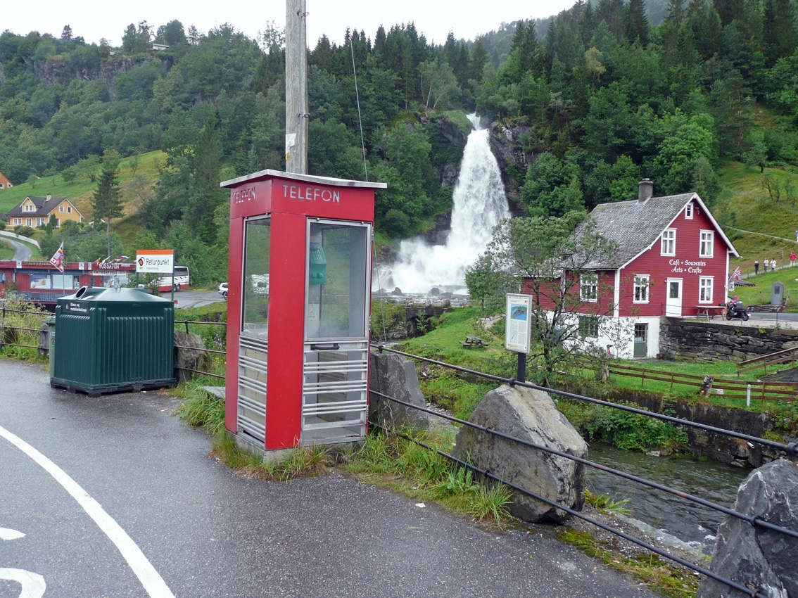 This is the story of how Norway’s most important conversation-space was designed by a young, freshly graduated man from Bergen.

“Norwegian architects are hereby invited…”
In the autumn of 1932, Oslo Telefonanlegginitiated an architectural competition. Finally, Oslo would get its own telephone booth. The city had had so called “talking-stations” from 1885, which in turn were overtaken by automatic telephones 
 only available at selected Narvesen kiosks. The state 
was of the opinion that now was the time to offer the public a better service; public telephone booths open 24/7, like the ones they already had in Sweden and England. But what would they look like, these new telephone booths? What considerations would it
 be necessary to take when designing it? The telegraph board developed a detailed list of demands and restraints: “The booth is intended to be placed outside on the streets and squares and need to be designed so that snow and ice does not hinder the opening and closing of the doors,” they wrote. “To prevent vandalism, theft, uncleanliness etc. inside the booth, it needs to be designed so that from all angles one may see what is going on in there.” Additionally, it would need to withstand storms and bad weather, and “preferably also being whipped by rain mixed with seawater” 

This was not all: The appearance would have to be «pleasing». The booth also needed to be movable, so that it could be taken in to be serviced at Telegrafverket’s main workshops. The reqired material was iron, and the surface was to be spray painted  preferably using car-body paint. There was a requirement for “a writing shelf, a pack shelf, and a suitable place for the telephone catalogue.” Also, there would need to be an illuminated TELEFON  sign, easily visible from all four angles. The total cost for each booth should not exceed 1000 kroner. The first prize for coming up with such a product was 800 kroner.

“Norwegianarchitects are hereby invited to partake in a competition for the design of a telephone booth…”  

The man with the solution
«At some point in 1932, Georg Fredrik sat at a party in Bergen. Maybe he felt a bit lost and forgotten as he often had throughout his life. He retreated to a quiet corner, took out a pencil and strted doodling on a matchbox.  According to my mother, this was how the telephone booth came into being.” In the book “Norges lille røde  historien om telefonkiosken,” Lars Fasting describes his father, the man who is far less known than the iconic architctural structure he left behind. Georg Fredrik Fasting was from Bergen, born into a family of working people and smallholders. One unusual facet of Georg Fredrik was that he was born without ears. His mother made sure he learnt to speak, read and write, 
ut Lars Fasting indicates that his father would seek refuge in drawing when the social challenges became too much to bear. And in the end drawing became his profession. In 1924 he secured a guarantor for a student loan, and started studying to become an a
rchitect at the NTH. Throughout the 1930s he entered several architectural competitions, with drafts produced, according to his son, “after work and in the late hours of the night.”

His efforts were not wasted. Out of 93 entries, with names such as “Flirt”, “Brrr”, “Ring” and “Amor”, the jury selected Fasting’s submission, “RIKS” as the new telephone booth: “The draft shows a strikingly simple solution to the task, technically as well as aesthetically well worked out.”

Taut and provident
Simple and aesthetc are the keywords here. Fasting had designed a booth pointing towards the future, and to modernism. Just how modern it was can be seen by comparing RIKS to the British telephone booth, also designed in the interwar-era. While the British version with it classicistic style is looking back to the heyday of the empire, Fasting’s booth is progressive and functionalistic. Like most Norwegian architects, Fasting broke with the classicistic style of architecture after the Stockholm-exhibition in 1930. “After it, almost all buildings erected in Norway until the German invasion in 1940, were in the functionalistic architectural style,” writes senior curator of architecture at the Norwegian National Museum, Ulf Grønvold, in the book, “Den lille røde”.“TheNorwegian booth is a piece of functionalistic architecture, an asymmetric composition with its roof slab overhanging the word TELEFON, in bold sans seraph lettering,”concludes Ulf Grønvold.

Fashionably red
And it was red. Fasting chose a colour which was part of the modern palette. “A bright red colour, but not as shiny as a signal red, the character of the colour places it among the fashionable colours within functionalism,” states paintings conservator and researcher in NIKU (Norwegian Institute for Cultural Heitage Research), Jon Brænne. In his opinion, Fasting went for visibility without making the booth stand out too much from its surroundings. The original colour was in use up to around 1950, when it changed to signal red. Towards the end of the 1970s the clour was again adjusted towards today’s orangey red.

The design, however, has not changed. RIKS is eighty years and still looks remarkably good. That’s what makes Fasting’s telephone booth a classic  even before it was added to DOCOMOMO’s list over moden icons of design. For Telenor, the telephone booth has served as a pathway into the hearts of the public. For many, Telenor (Televerket) was synonymous with exactly this telephone booth, because this was where one would go to place a call. Having a home
phone was not common until the 1980s. As such the red box became part of the Norwegian everyday and consciousness. The symbol- and publicity value of this is hard to evaluate, but in 2007 it was time to give honour where honour was due, Telenor, in consul
tation with the Directorate for Cultural Heritage, decided to preserve 100 telephone booths for all eternity.

And what about Georg Fredrik Fasting? What happened to him? At the age of 56 an entry in his diary states: «I CAN HEAR». As the first person in th world he had undergone an operation where he had ear canals constructed and eardrums fitted. For the rest of his life, the man behind Norway’s own telephone booth could answer the telephone himself.

Source: Norges lille røde historien om telefonkiosken (2007), issued by The Norwegian Telecom Museum and Telenor Cultural Heritage.
