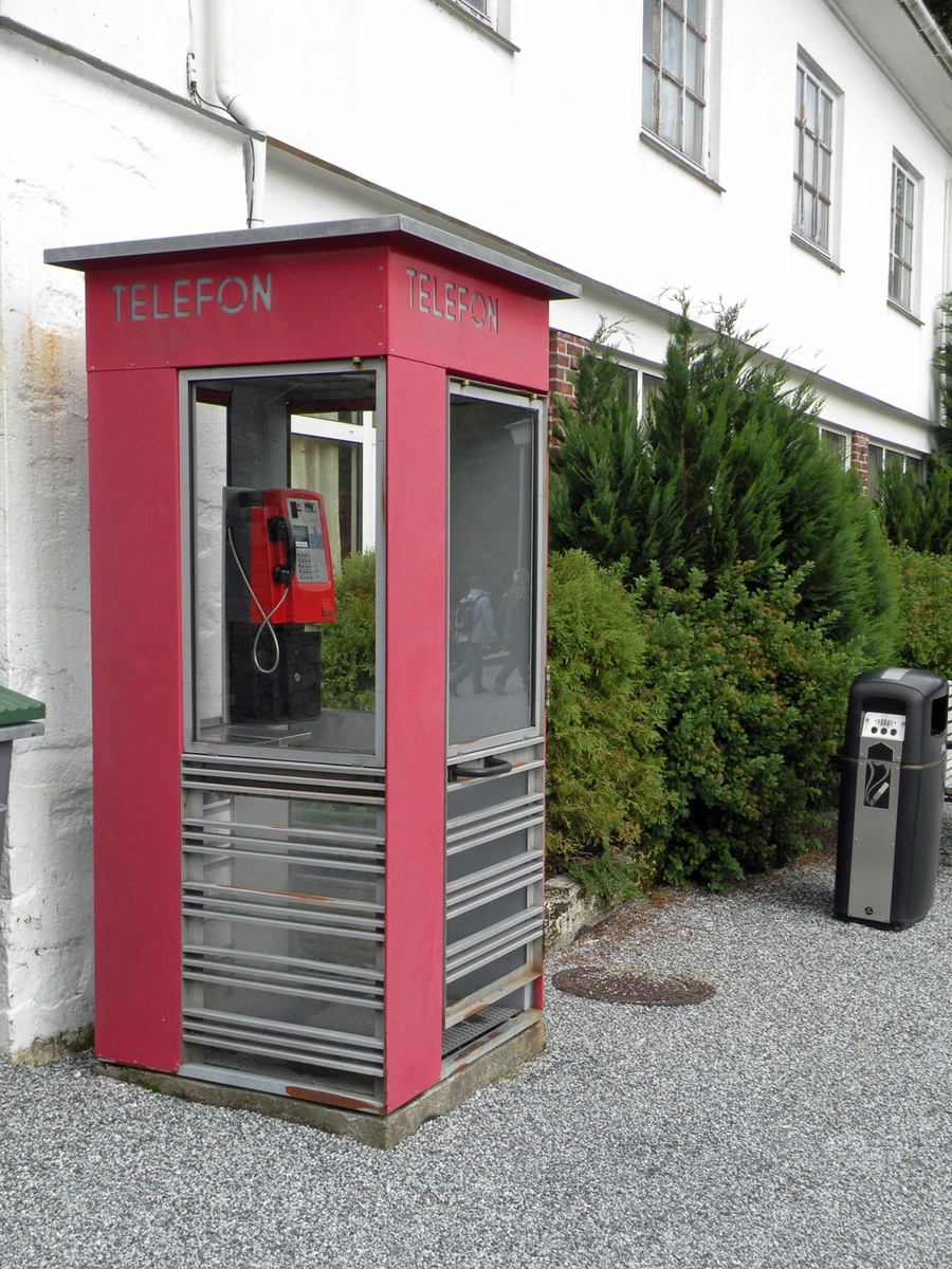This is the story of how Norway’s most important conversation-space was designed by a young, freshly graduated man from Bergen.

“Norwegian architects are hereby invited…”
In the autumn of 1932, Oslo Telefonanlegginitiated an architectural competition. Finally, Oslo would get its own telephone booth. The city had had so called “talking-stations” from 1885, which in turn were overtaken by automatic telephones 
 only available at selected Narvesen kiosks. The state 
was of the opinion that now was the time to offer the public a better service; public telephone booths open 24/7, like the ones they already had in Sweden and England. But what would they look like, these new telephone booths? What considerations would it
 be necessary to take when designing it? The telegraph board developed a detailed list of demands and restraints: “The booth is intended to be placed outside on the streets and squares and need to be designed so that snow and ice does not hinder the opening and closing of the doors,” they wrote. “To prevent vandalism, theft, uncleanliness etc. inside the booth, it needs to be designed so that from all angles one may see what is going on in there.” Additionally, it would need to withstand storms and bad weather, and “preferably also being whipped by rain mixed with seawater” 

This was not all: The appearance would have to be «pleasing». The booth also needed to be movable, so that it could be taken in to be serviced at Telegrafverket’s main workshops. The reqired material was iron, and the surface was to be spray painted  preferably using car-body paint. There was a requirement for “a writing shelf, a pack shelf, and a suitable place for the telephone catalogue.” Also, there would need to be an illuminated TELEFON  sign, easily visible from all four angles. The total cost for each booth should not exceed 1000 kroner. The first prize for coming up with such a product was 800 kroner.

“Norwegianarchitects are hereby invited to partake in a competition for the design of a telephone booth…”  

The man with the solution
«At some point in 1932, Georg Fredrik sat at a party in Bergen. Maybe he felt a bit lost and forgotten as he often had throughout his life. He retreated to a quiet corner, took out a pencil and strted doodling on a matchbox.  According to my mother, this was how the telephone booth came into being.” In the book “Norges lille røde  historien om telefonkiosken,” Lars Fasting describes his father, the man who is far less known than the iconic architctural structure he left behind. Georg Fredrik Fasting was from Bergen, born into a family of working people and smallholders. One unusual facet of Georg Fredrik was that he was born without ears. His mother made sure he learnt to speak, read and write, 
ut Lars Fasting indicates that his father would seek refuge in drawing when the social challenges became too much to bear. And in the end drawing became his profession. In 1924 he secured a guarantor for a student loan, and started studying to become an a
rchitect at the NTH. Throughout the 1930s he entered several architectural competitions, with drafts produced, according to his son, “after work and in the late hours of the night.”

His efforts were not wasted. Out of 93 entries, with names such as “Flirt”, “Brrr”, “Ring” and “Amor”, the jury selected Fasting’s submission, “RIKS” as the new telephone booth: “The draft shows a strikingly simple solution to the task, technically as well as aesthetically well worked out.”

Taut and provident
Simple and aesthetc are the keywords here. Fasting had designed a booth pointing towards the future, and to modernism. Just how modern it was can be seen by comparing RIKS to the British telephone booth, also designed in the interwar-era. While the British version with it classicistic style is looking back to the heyday of the empire, Fasting’s booth is progressive and functionalistic. Like most Norwegian architects, Fasting broke with the classicistic style of architecture after the Stockholm-exhibition in 1930. “After it, almost all buildings erected in Norway until the German invasion in 1940, were in the functionalistic architectural style,” writes senior curator of architecture at the Norwegian National Museum, Ulf Grønvold, in the book, “Den lille røde”.“TheNorwegian booth is a piece of functionalistic architecture, an asymmetric composition with its roof slab overhanging the word TELEFON, in bold sans seraph lettering,”concludes Ulf Grønvold.

Fashionably red
And it was red. Fasting chose a colour which was part of the modern palette. “A bright red colour, but not as shiny as a signal red, the character of the colour places it among the fashionable colours within functionalism,” states paintings conservator and researcher in NIKU (Norwegian Institute for Cultural Heitage Research), Jon Brænne. In his opinion, Fasting went for visibility without making the booth stand out too much from its surroundings. The original colour was in use up to around 1950, when it changed to signal red. Towards the end of the 1970s the clour was again adjusted towards today’s orangey red.

The design, however, has not changed. RIKS is eighty years and still looks remarkably good. That’s what makes Fasting’s telephone booth a classic  even before it was added to DOCOMOMO’s list over moden icons of design. For Telenor, the telephone booth has served as a pathway into the hearts of the public. For many, Telenor (Televerket) was synonymous with exactly this telephone booth, because this was where one would go to place a call. Having a home
phone was not common until the 1980s. As such the red box became part of the Norwegian everyday and consciousness. The symbol- and publicity value of this is hard to evaluate, but in 2007 it was time to give honour where honour was due, Telenor, in consul
tation with the Directorate for Cultural Heritage, decided to preserve 100 telephone booths for all eternity.

And what about Georg Fredrik Fasting? What happened to him? At the age of 56 an entry in his diary states: «I CAN HEAR». As the first person in th world he had undergone an operation where he had ear canals constructed and eardrums fitted. For the rest of his life, the man behind Norway’s own telephone booth could answer the telephone himself.

Source: Norges lille røde historien om telefonkiosken (2007), issued by The Norwegian Telecom Museum and Telenor Cultural Heritage.