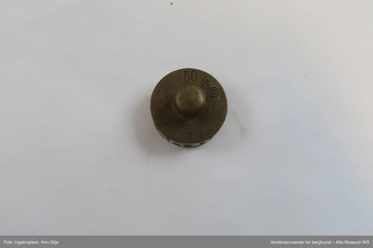 Rektangulær trebit, med hull tilpasset ulike loddstørrelser. Det er 7 lodd: 2 stk. 10 gram, 1 stk. 20 gram, 1 st. 50 gram, 2 stk. 100 gram og 1 stk. 200 gram. Alle loddene er sylinderformet med knott på toppen. Loddene varierer i størrelse: de minste er 2 cm i diameter og 1 cm i høyde, mens den største er 4 cm i diameter og 2,8 cm i høyde.