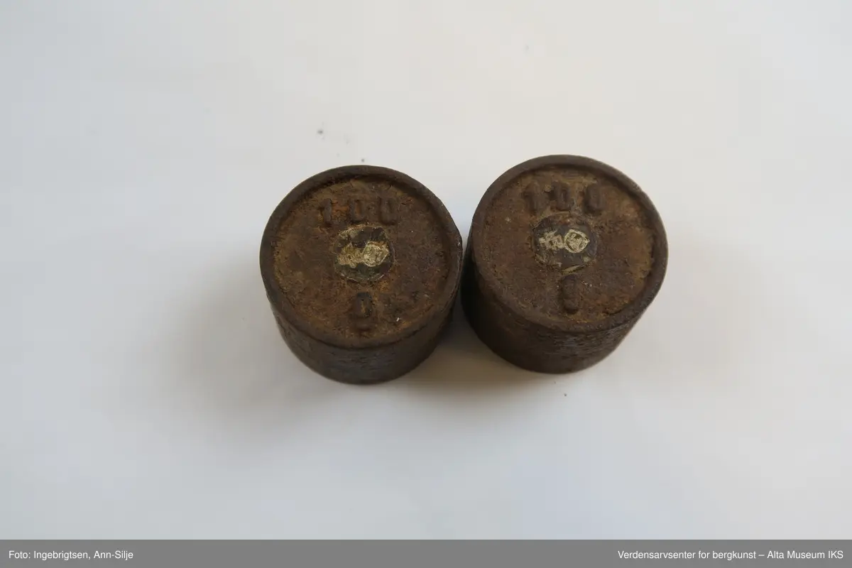Rektangulær trebit, med hull tilpasset ulike loddstørrelser. Det er 7 lodd: 2 stk. 10 gram, 1 stk. 20 gram, 1 st. 50 gram, 2 stk. 100 gram og 1 stk. 200 gram. Alle loddene er sylinderformet med knott på toppen. Loddene varierer i størrelse: de minste er 2 cm i diameter og 1 cm i høyde, mens den største er 4 cm i diameter og 2,8 cm i høyde.