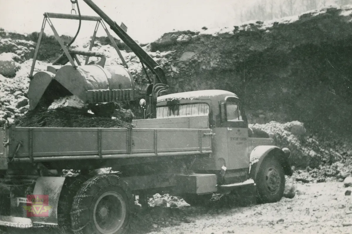 Volvo lastebil og grabb. Knyttes til bilde NVM 00-F-34031. Colbjørnsen med flere beskuer det hele.