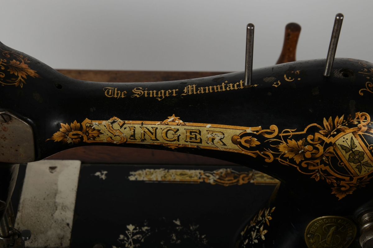 Symaskin med bord og lokk. Understell av støpejern, med pedal.

Treflaten som symaskinen står på har innfelte hull til å sette lokket i. En liten trebit står i et hull i bordet.