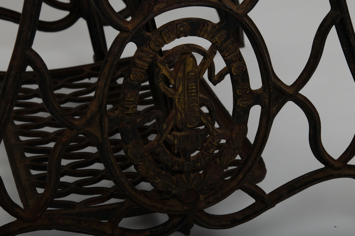 Symaskin med bord og lokk. Understell av støpejern, med pedal.

Treflaten som symaskinen står på har innfelte hull til å sette lokket i. En liten trebit står i et hull i bordet.