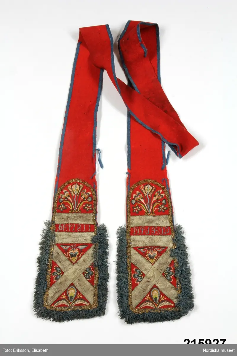 "Brudlist, röd vadmal, kantad med blått siden, i båda ändar broderier i flera färger silke, applikation av guldband och guldspetser, frans av silka; märkt MPS/AHP 1811"
/enligt intendent Inga Wintzells anteckningar