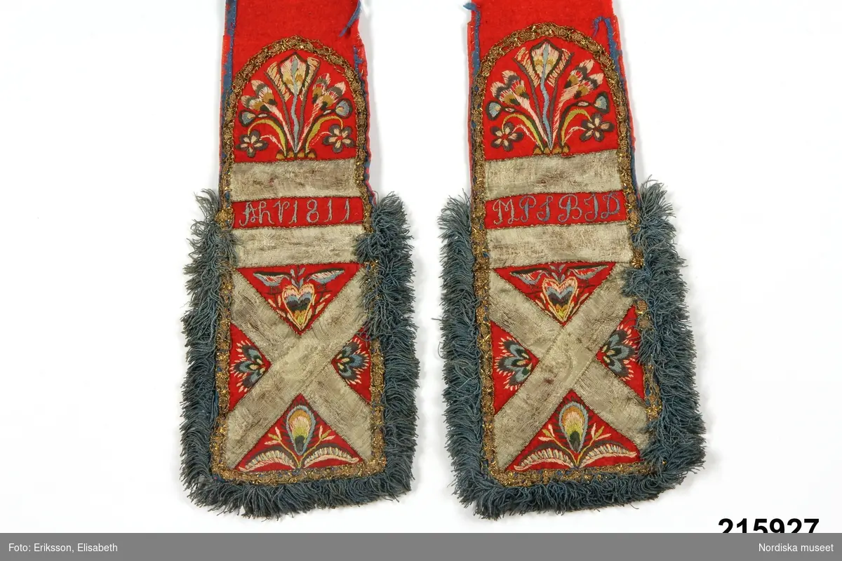 "Brudlist, röd vadmal, kantad med blått siden, i båda ändar broderier i flera färger silke, applikation av guldband och guldspetser, frans av silka; märkt MPS/AHP 1811"
/enligt intendent Inga Wintzells anteckningar