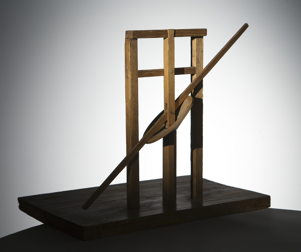 Modell ur Polhems mekaniska alfabet. Text på föremålet: "LXIV". Vid rotation av den lodräta axeln erhålles med hjälp av den vinkelställda skivan en vickande rörelse hos armen.