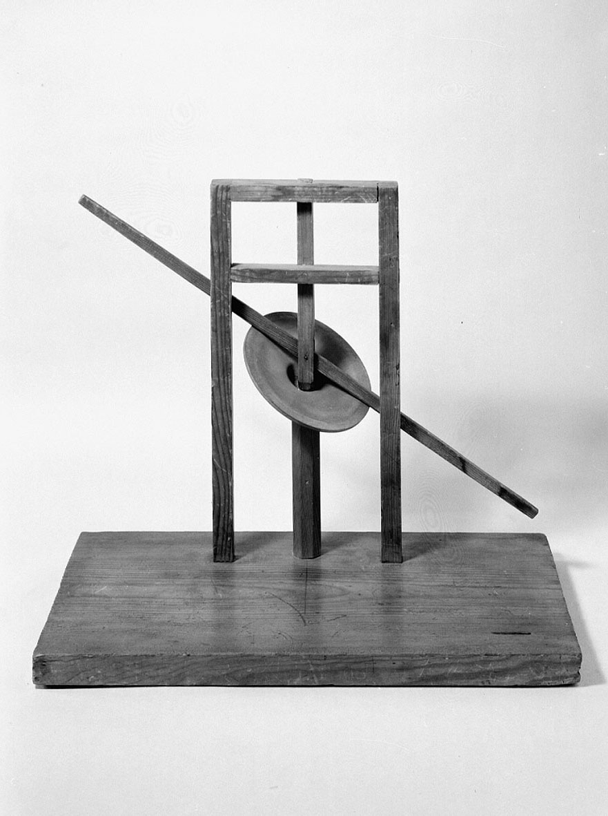 Modell ur Polhems mekaniska alfabet. Text på föremålet: "LXIV". Vid rotation av den lodräta axeln erhålles med hjälp av den vinkelställda skivan en vickande rörelse hos armen.