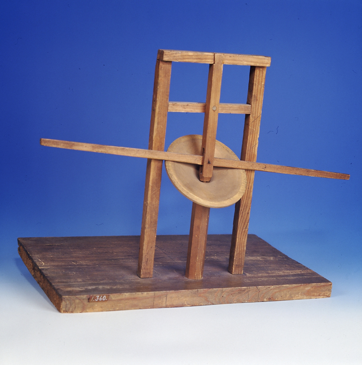 Modell ur Polhems mekaniska alfabet. Text på föremålet: "LXIV". Vid rotation av den lodräta axeln erhålles med hjälp av den vinkelställda skivan en vickande rörelse hos armen.