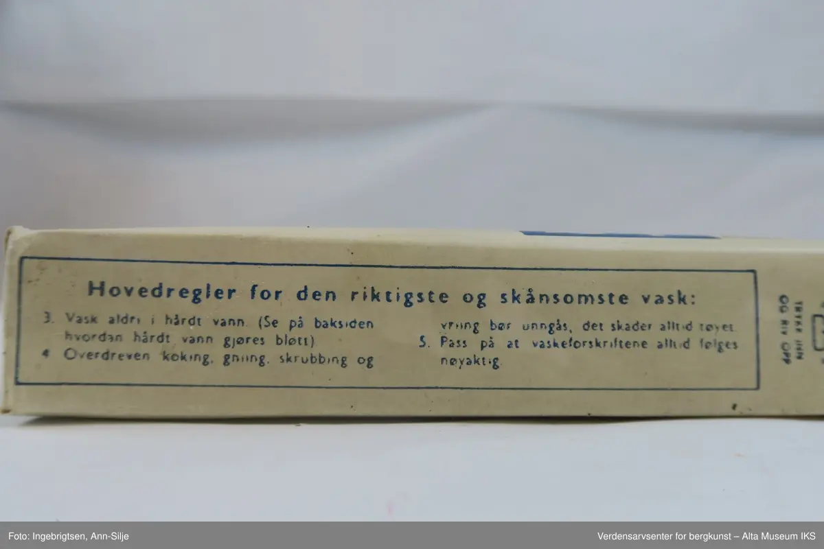 Hvit rektangulær pakke med pulver. Øverst på pakkens forside er det et blått felt med hvit skrift. Ellers er det tekst i blått skrevet på alle sidene på pakken.