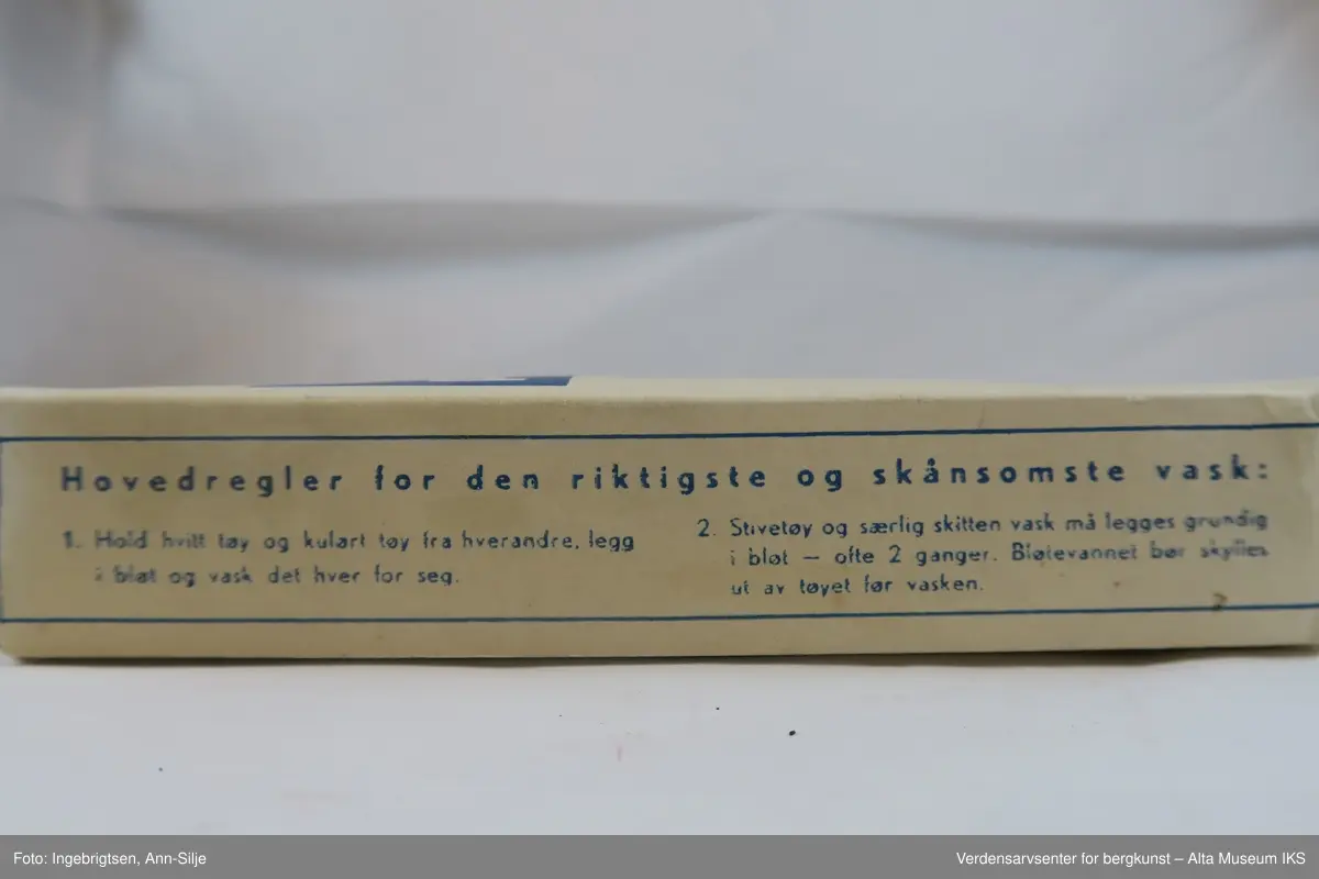 Hvit rektangulær pakke med pulver. Øverst på pakkens forside er det et blått felt med hvit skrift. Ellers er det tekst i blått skrevet på alle sidene på pakken.