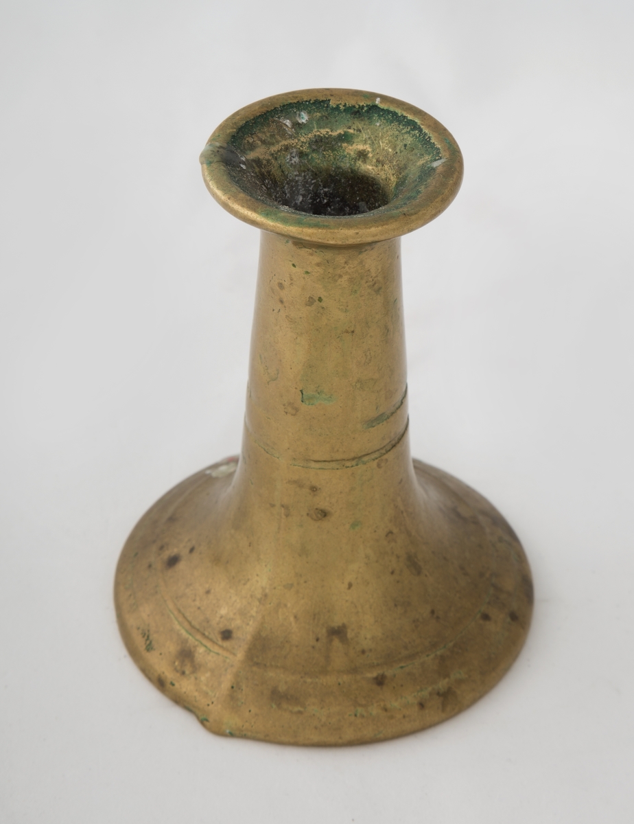 Rund sokkel, slank utføring. Dekorert med to riller på sokkel, og to riller på skaftet. Vider seg ut ved lyspipen.