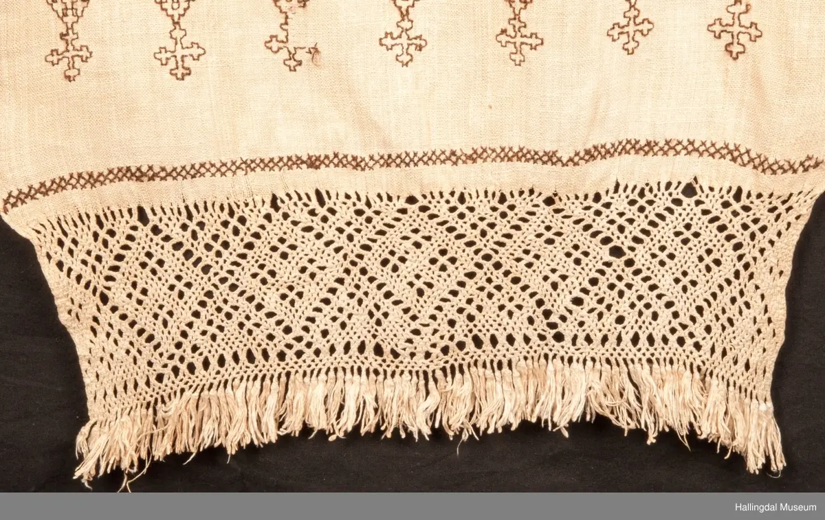 Tilnærmet rektangulært stk. hvit linlerret, håndvevet. Jarekanter i langsidene, faldet for hånd i ei kortside. Det vevde stykket ca. 130 cm langt og fortsetter i en knipling i firflettingsteknikk av renningstrådene. På linet er brodert mønster m/ 2-tråds, håndspunnet, mørk brunt ullgarn. Geometriske mønster i holbeinsting og korssting, nær falden er brodert 3 bokstaver (siste er D, to første er usikre) og årstallet 1757 i korssting og kjedessting.