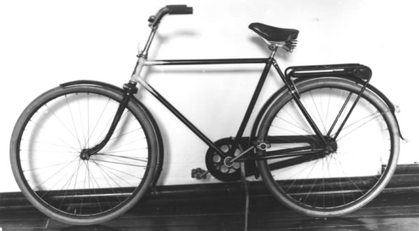Cykel av stålrör. Herrmodell. Tillverkad av Husqvarna Vapenfabrik AB. Lädersadel, utdragbar vertygslåda av plåt under pakethållaren liksom hållare för pump. Lås, ringklocka och däck ej original. Vinrödfärgat lack, gräddgul dekor.
