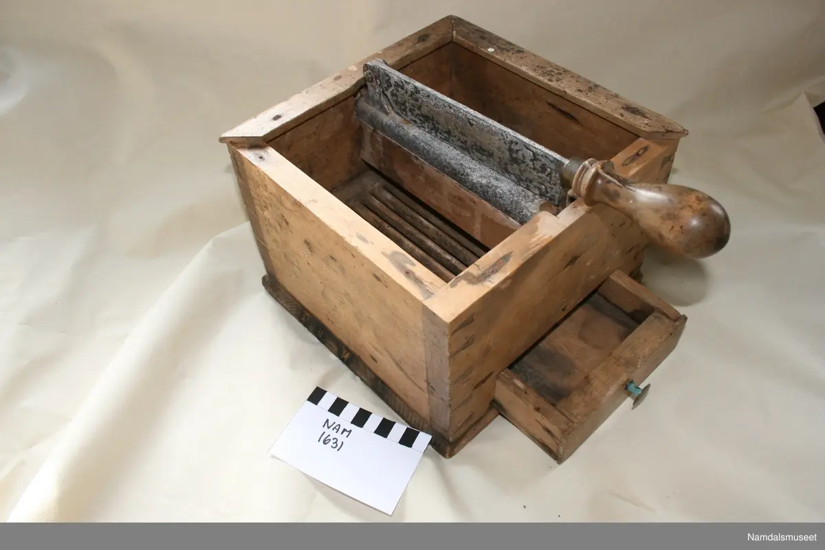 Teknikk: Sinket trekasse med skuffer. Lister på oversiden. På en jernbeslått midtstolpe er hengslet en kniv med trehandtak.
Avdelt med trerist og skuffe under.
Form: Kvadratisk kasse.
