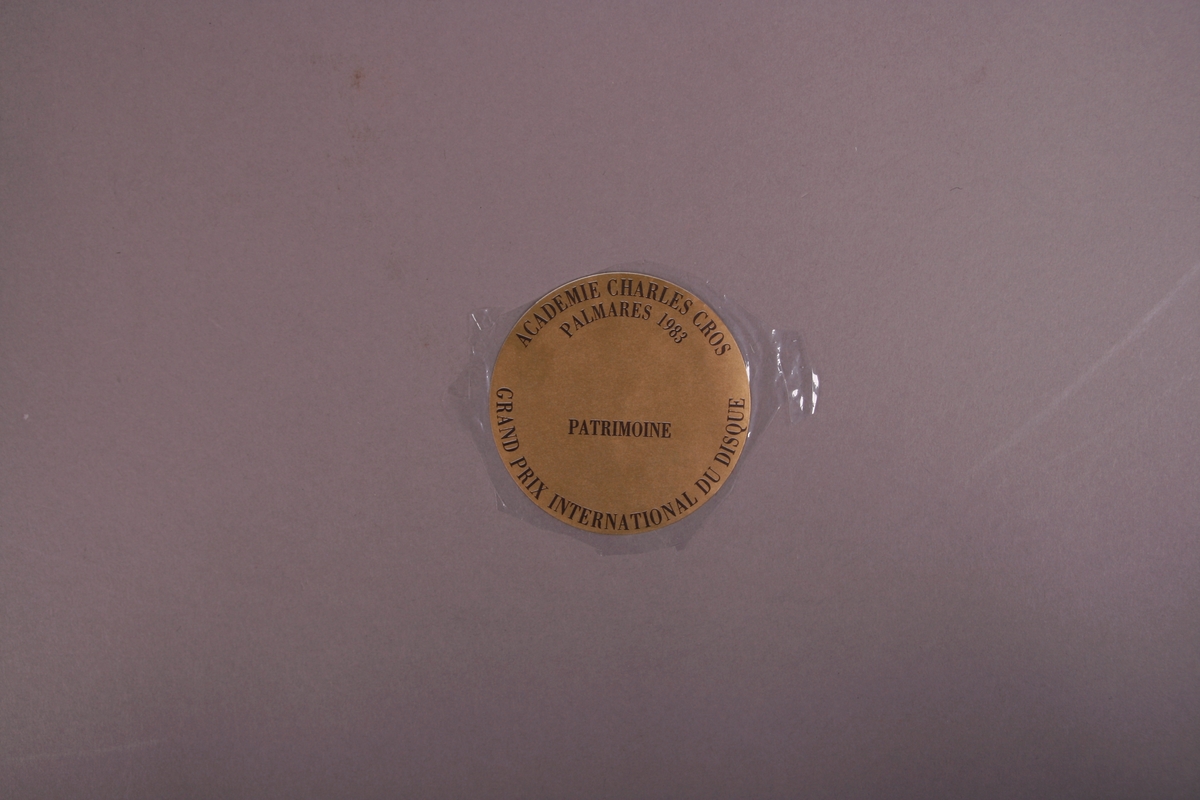 Plateomslag i form av en eske i oransje stoff, tre grammofonplater i svart vinyl som ligger i papirlommer, samt et hefte. I tillegg et klistremerke inne i  esken.