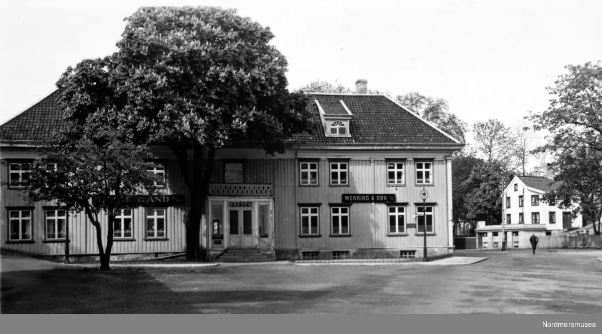 Et bilde fra Børsen i Johnsengården ved Johnsenhuken, med skilt for klippfiskeksportør Werring & Søn, men  uten Christie-støtten foran. Denne støtten har stått på flere forskjellige plasser på Kirkelandet i Kristiansund gjennom tidene, blant annet en periode utenfor Johnsengården, der han ble født. Per 2008 står støtten i enden av Christies gate ved Brannstasjonen. Fra Nordmøre Museums fotosamlinger. 
