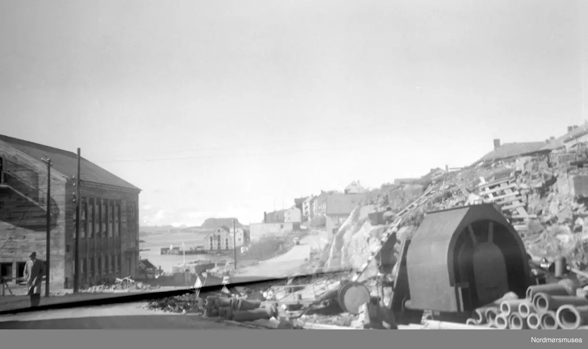 På bildet ser vi Storgata, sett fra den gamle "Svineryggen" mot vest.  Til høyre ser vi en del av en tysk bunker fra krigen. Til venstre Handelens Hus/Børsen og firmaet Hoem & Hoel. I bakgrunnen Sørholmen og  Bremsneshatten i det fjerne. Nordmøre Museums fotosamling