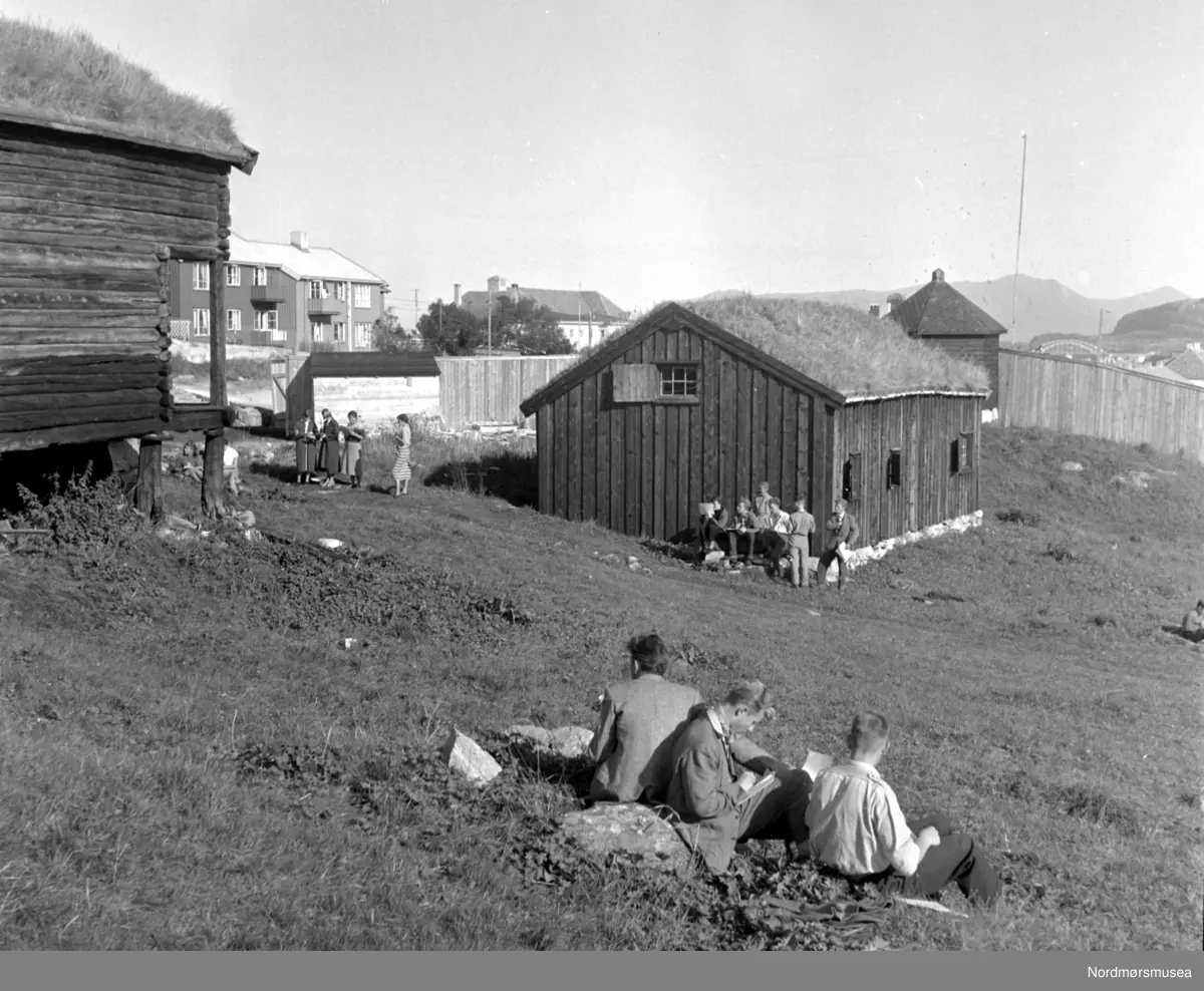 Almskårstua i Clausenenga før flytting til Knudtzondalen.
Røykstua (midten), litt av stabburet til venstre og "Vardetårnet fra 1808" i bakgrunnen.  Viser en studietur med frihandstegning og omvisning for en klasse av Kristiansund offentlige høyere allmenskole.  En varm og soleklar septemberdag.
(Frå Nordmøre Museum si fotosamling) duplikat