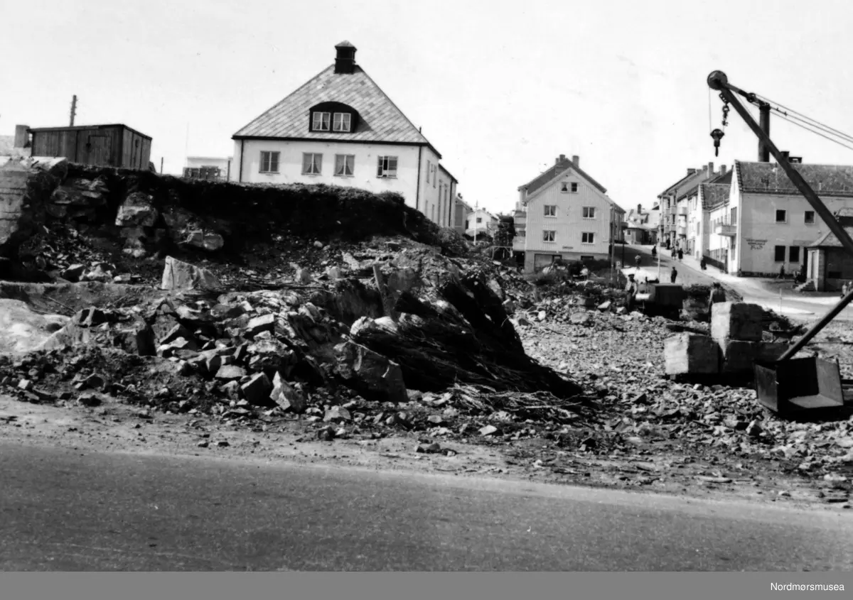 På bildet ser vi siste rest av fjellhaugen, der Arbeiderforeningen og Rådstua stod. I bakgrunnen ser vi rester av en tysk "bunkers" som ble bygget under krigen, og over denne bunkersen hadde da Arbeiderforeningen stått før bybrannen i de sene aprildagene 1940. Bak denne igjen ser vi nåværende bygg for folkebiblioteket. I bakgrunnen ser vi Indremisjonsbygget og utover Marstrands gate. På 60-tallet var Lastebilsentralen her. Nordmøre Museums fotosamling