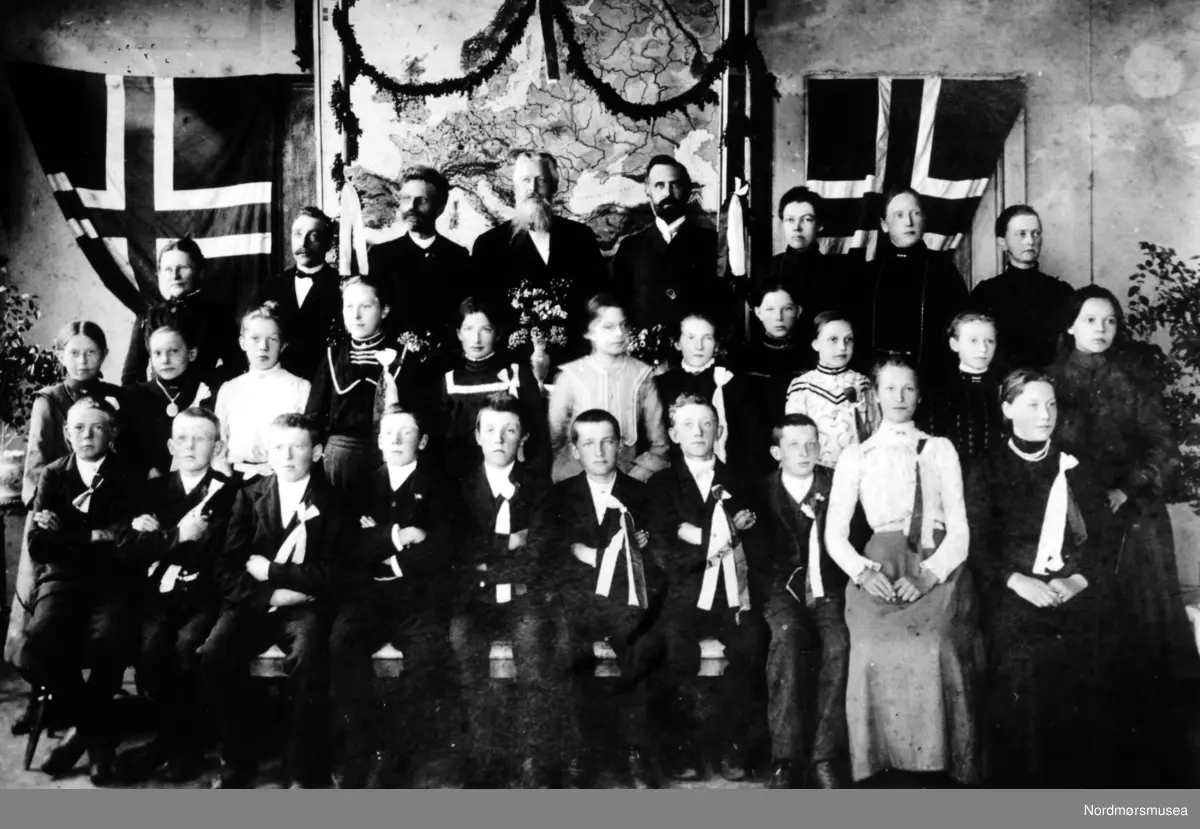 Nordlandet folkeskole, Kristiansund. Mannen med bart øverst til venstre er min oldefar Erling Kvendbø som var lærer. Han flyttet til Nordlandet i 1899. Han var født i 1867 i Surnadal og døde i 1938.  Dette er et bilde av avgangsklassen ca 1905. Det bildet jeg har er avgangsklassen i 1908, og dette bildet må være tatt noen år før pga. 2 ting: Erling Kvendbø ser litt yngre ut her, og det bildet jeg har, er av bedre kvalitet - skarpere med mer.    Info fra 
Astrid Kvendbø 2017 . -   lærere og elever ved en høytidelig anledning. I bakgrunnen kan man se et kart over Europa og det norske flagg.
 Fra Nordmøre Museums samlinger.