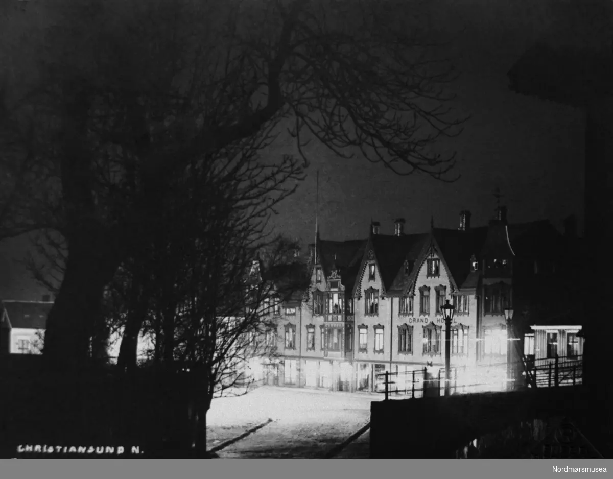 Postkort:  ";Christiansund N.  Foto ved lukslys af O. R.";  Grand Hotel ved natt, på Torvet, Kirkelandet, Kristiansund. (Fra Nordmøre Museum sin fotosamling.) /Reg:EFR2013/



