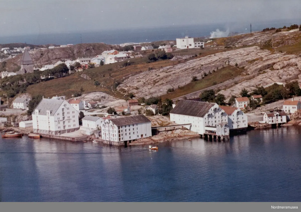 Nordlandet, Kirka opp i venstre hjørne, T . H. Øverlands klippfiskbrygge midt på bildet. Den er pr 2008 brent ned. Datering er 11. juli 1962.  Fra Nordmøre museums fotosamlinger.
