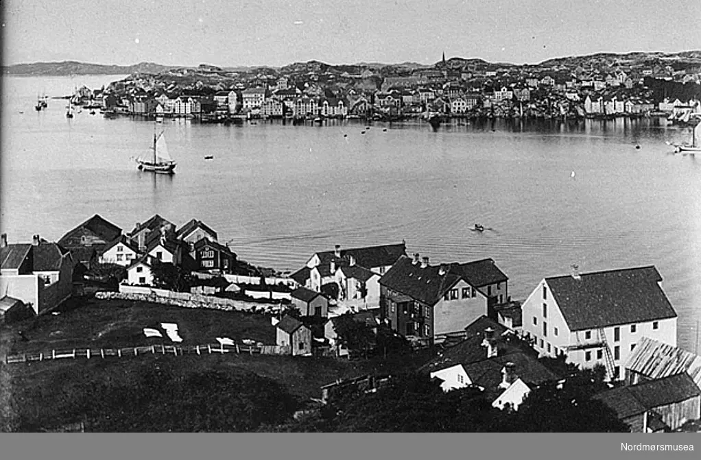 Katalog over bilder av eldre gateparti, bygninger og bygningsdetaljer i Kristiansund. Bildene er bekostet av Det Kulturhistoriske Lag (DKL)og med bidrag av Kristiansund Sparebank og fru Caroline Knudtzon. Ført i protokoll av overlærer Wilhelm Lund. Foto hovedsakelig utført av fotograf Ole Olsen Ranheimsæter dersom ikke noe annet er anført. Tegninger utført av billedhugger J. Johnsen og Ole Ranheimsæter. DKL - er en forløper for Nordmøre Historielag, i tett samarbeid med Kristiansunds museum. Nr. 55 Postkort merket: ";Christiansund Panorama II";. Parti av Kristiansund, alle land. Signert Axel Lindahl. I forgrunden Nordlandet. Da byens nye kirke sees paa billedet, maa dette ifølge H. M. Neeraas være fotografert efter 1878. Se kmb-1982-024.0055a Fra Nordmøre Museum sin fotosamling.
