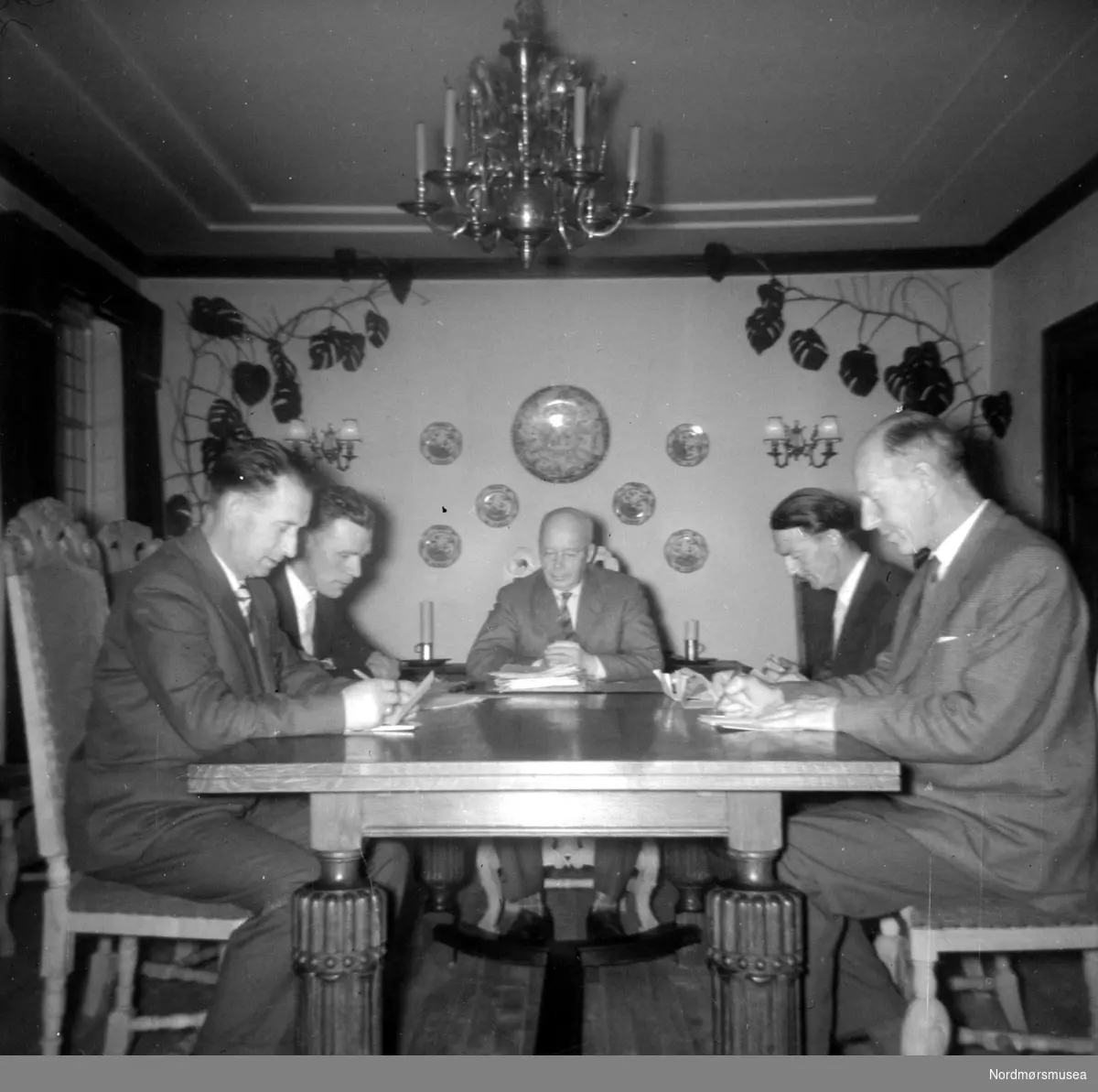 Foto muligens fra et arbeidsmøte? Her ser vi en gruppe menn sittende rundt et bord. Fotograf er ukjent, men kan være fra Fasting familien eller deres omgangskrets. Fotoserie. Fotografier gitt til Nordmøre Museum fra Kate og Kristian Fastings arvinger per 1986. Fra Nordmøre Museums fotosamlinger. 