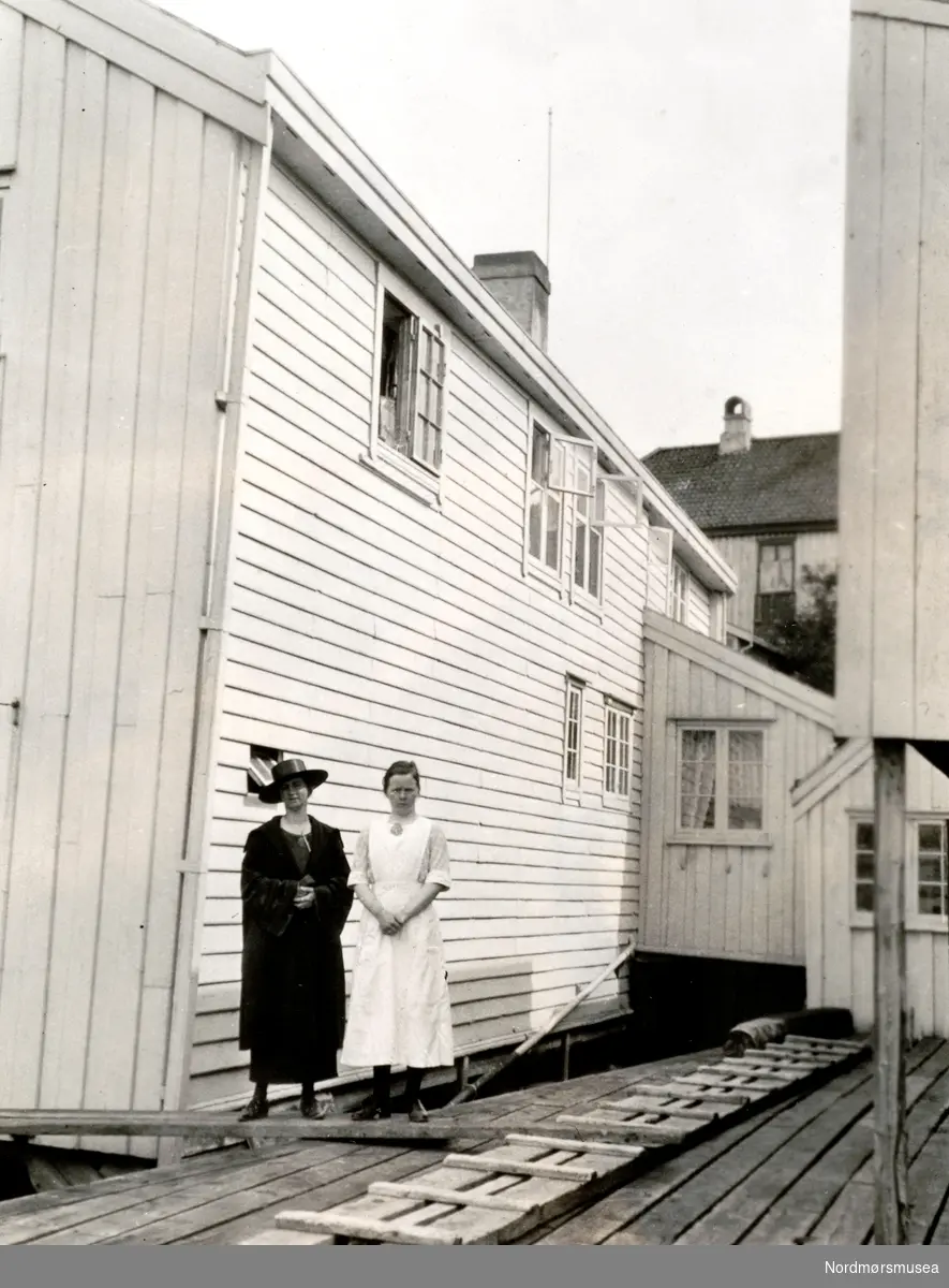 Foto fra Grunden 33 (bygget til venstre. Grunden 31 til høyre) på Nordlandet i Kristiansund, hvor vi ser Fru Astrid Rosenvold, her trolig sammen med en tjenestepike. Bildet er datert 1924, fotograf er ukjent. Følgende tekst er skrevet på baksiden: ";Til(?) syd+vestre fl&ouml;i av 2 etage før ombygning i 1929. Der var snedker verksted i det rum som har vindu med de små ruter."; Fra Nordmøre Museums fotosamlinger. Reg: EFR
