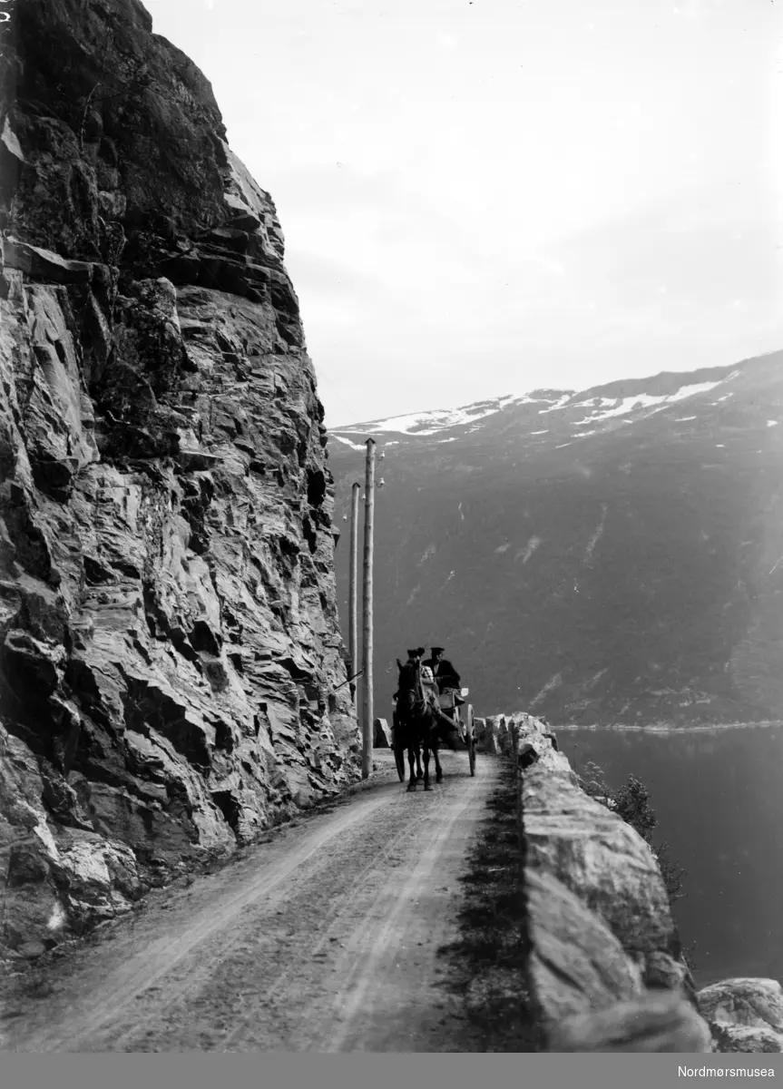 Hest og kjerre langs en grusvei, hvor vi ser sjøen på den ene siden og den bratte fjellsiden på den andre. Kan dette være fra strekningen Kvisvik-Gyl i Tingvoll kommune? Fotograf er trolig Georg Sverdrup. Datering er sannsynligvis omkring 1931. Se forøvrig KMb-1987-005.3690. Fra Nordmøre museums fotosamlinger.

