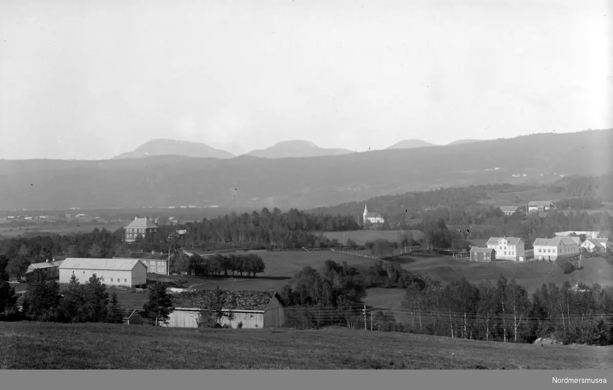 Fra Nordmøre Museum sin fotosamling. - Skei i Surnadal. I forgrunnen ser en uthusene til gården Fjellbu. Litt bak og til venstre ser en gården Skei. Bak denne er Doktorgården med valmet tak. Bak til høyre er Øye kirke. Helt til høyre i bildet ligger kommunehuset. Bak dette ligger Prestegården. I bakgrunnen er Nordmarka. Bak denne igjen stikker fjelltoppene Hjelmen, Hjelmkona og Saufjellet opp. (Informant: Ronny Bolgen.)



