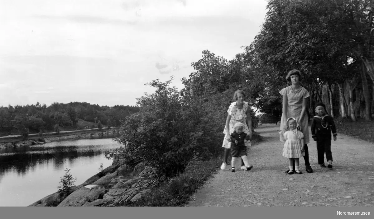 Foto av to unge kvinner, her sammen med tre små barn. Usikkert hvor, men antageligvis ved Vanndamman på Kirkelandet i Kristiansund. De unge kvinnene og barna er trolig fra Sverdrupfamilien/slekten, eller fra deres bekjentskaper. Datering er trolig omkring 1915 til 1930. Fra Nordmøre museums fotosamlinger. Reg: EFR
